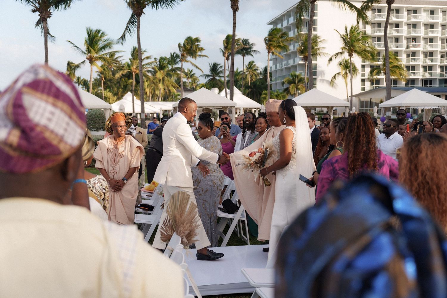 Wedding celebration on a tropical beach setup with palm trees and white tents in the background.
