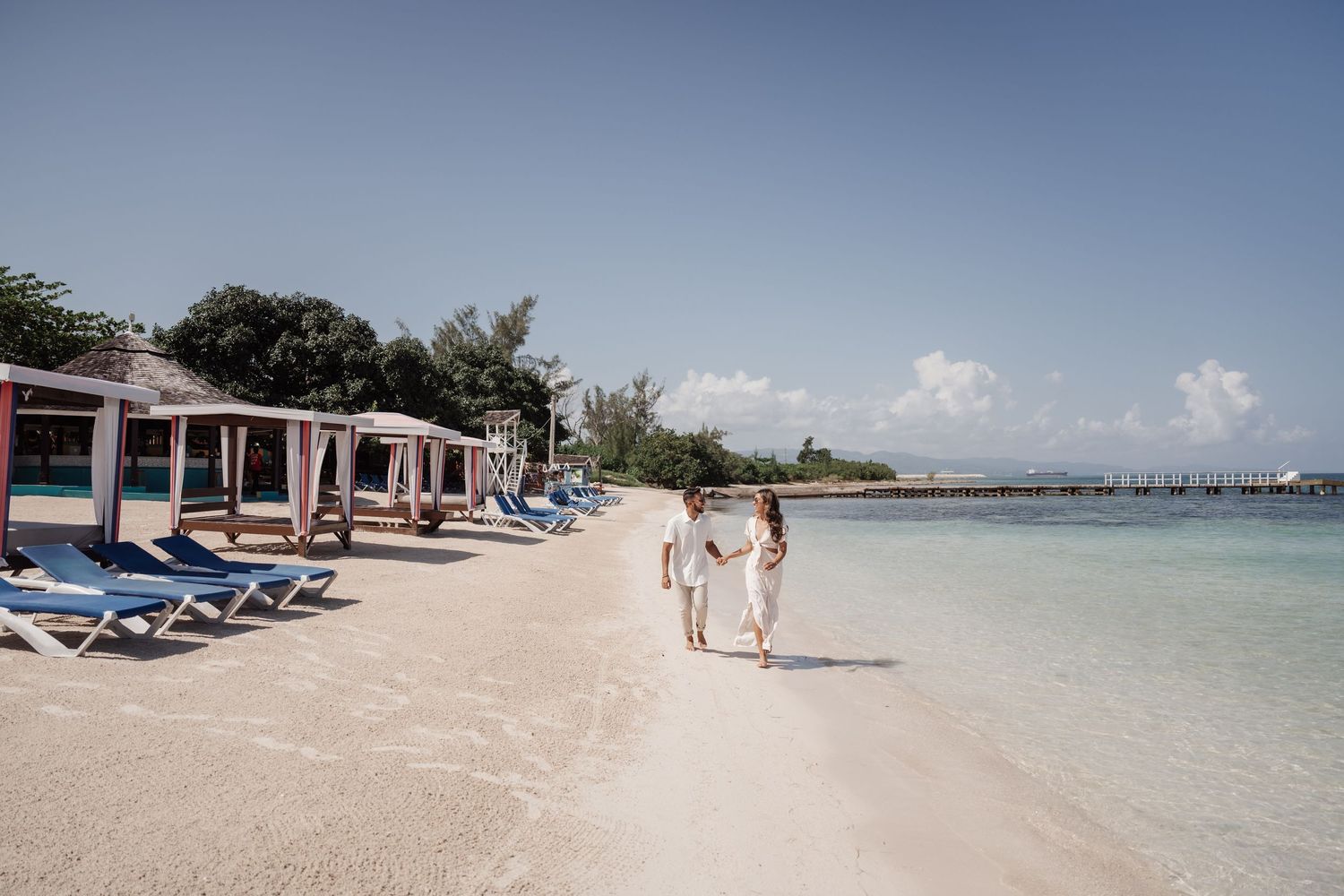 A distant view of a beach resort with lounge chairs and a couple walking along the shoreline.