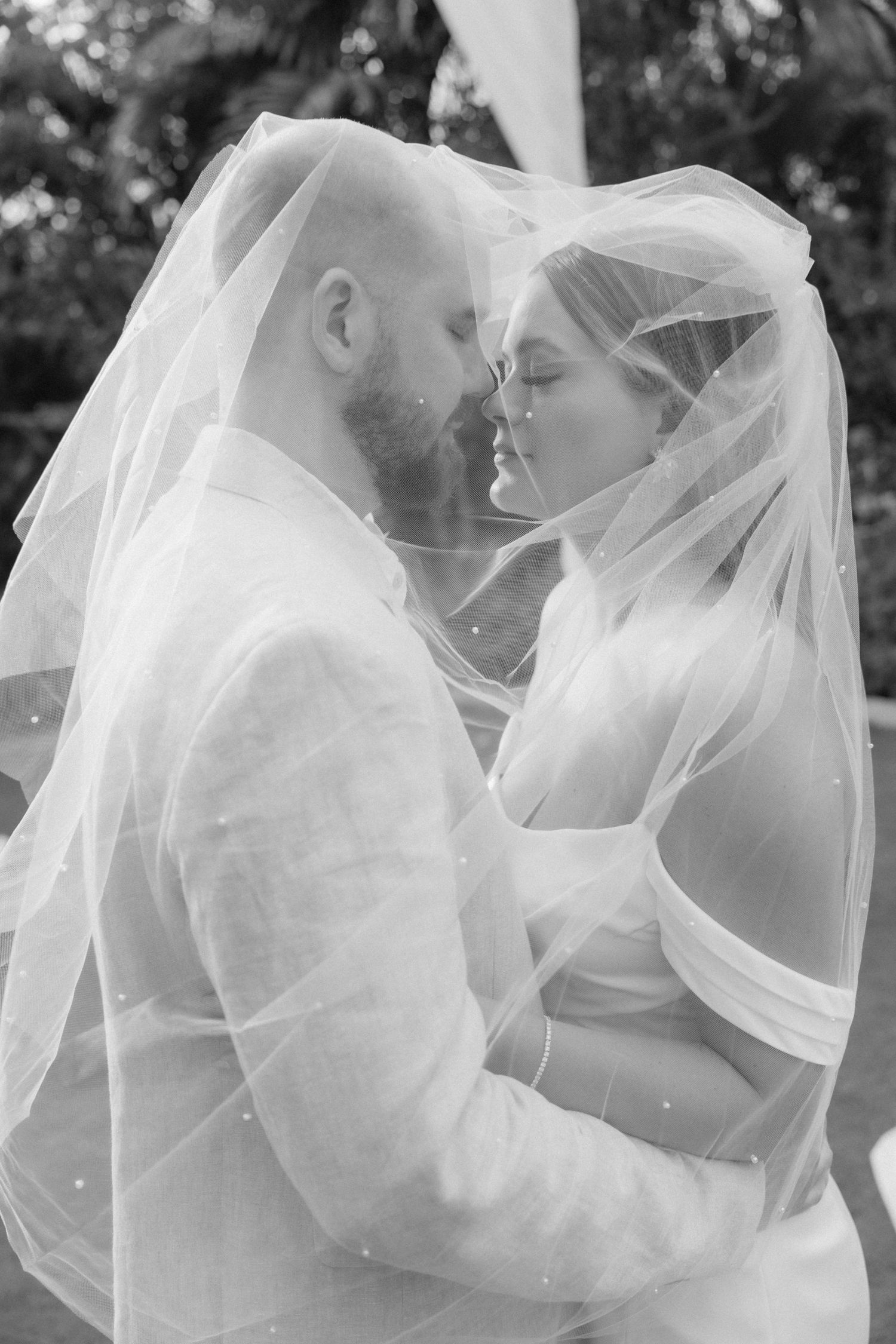 Romantic black and white portrait of couple embracing under wedding veil.