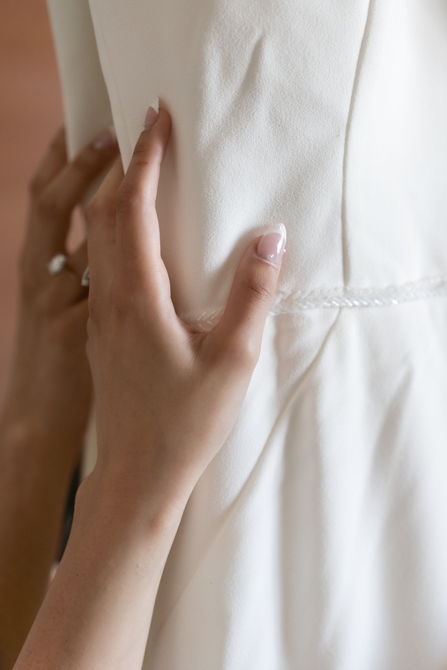 Close-up of delicate hand touching white wedding dress fabric, showing engagement ring.