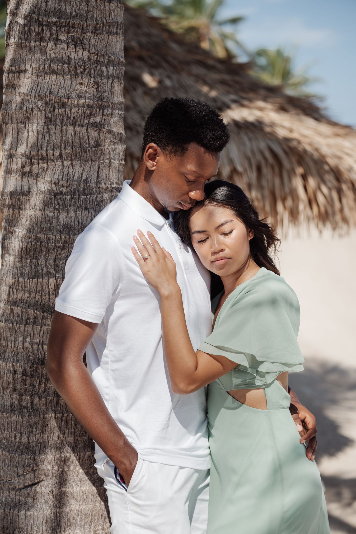 A couple shares an intimate moment against a palm tree on a tropical beach.