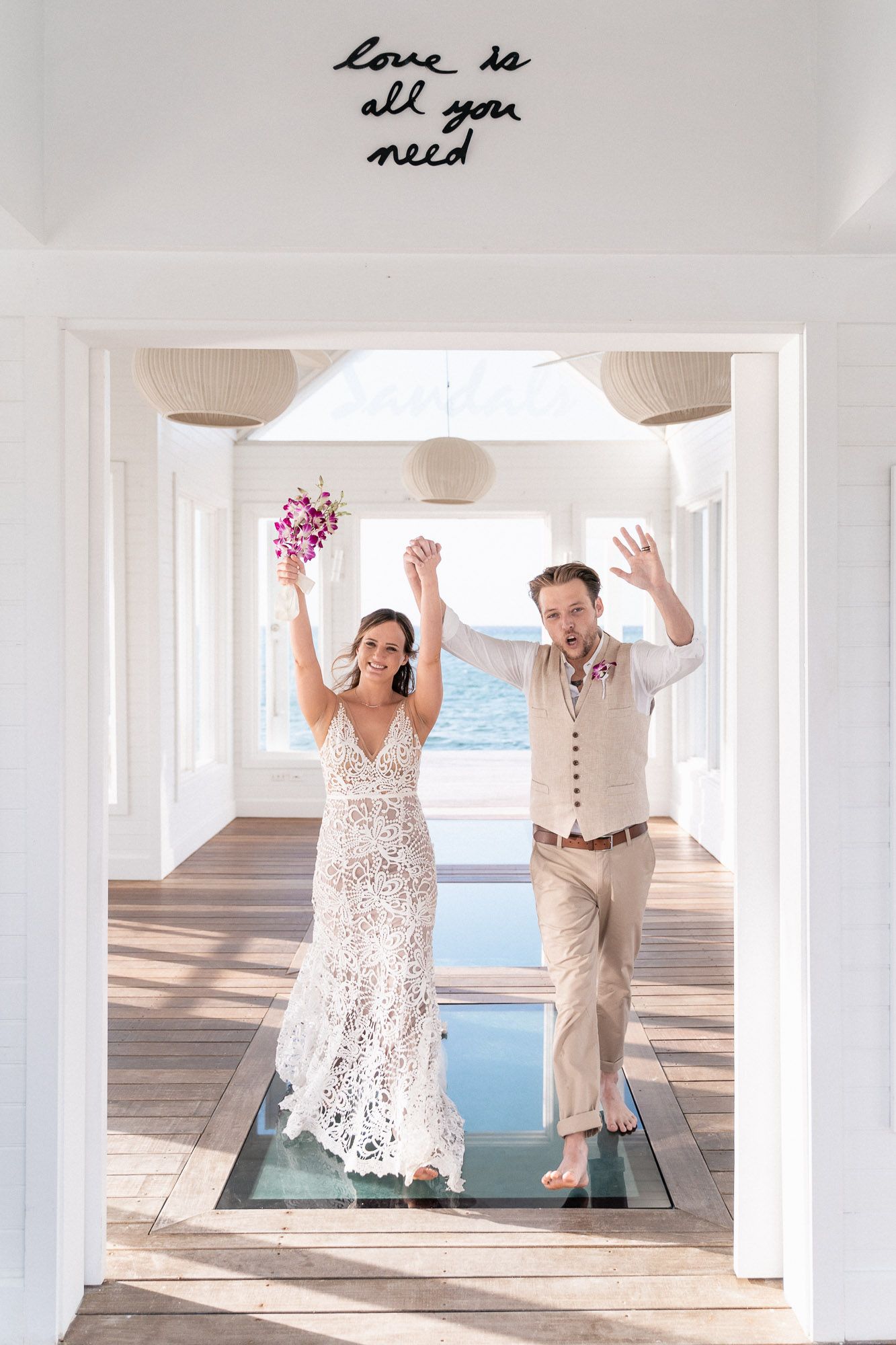 Celebrating newlyweds on glass walkway under sign reading 'Love is all you need'.