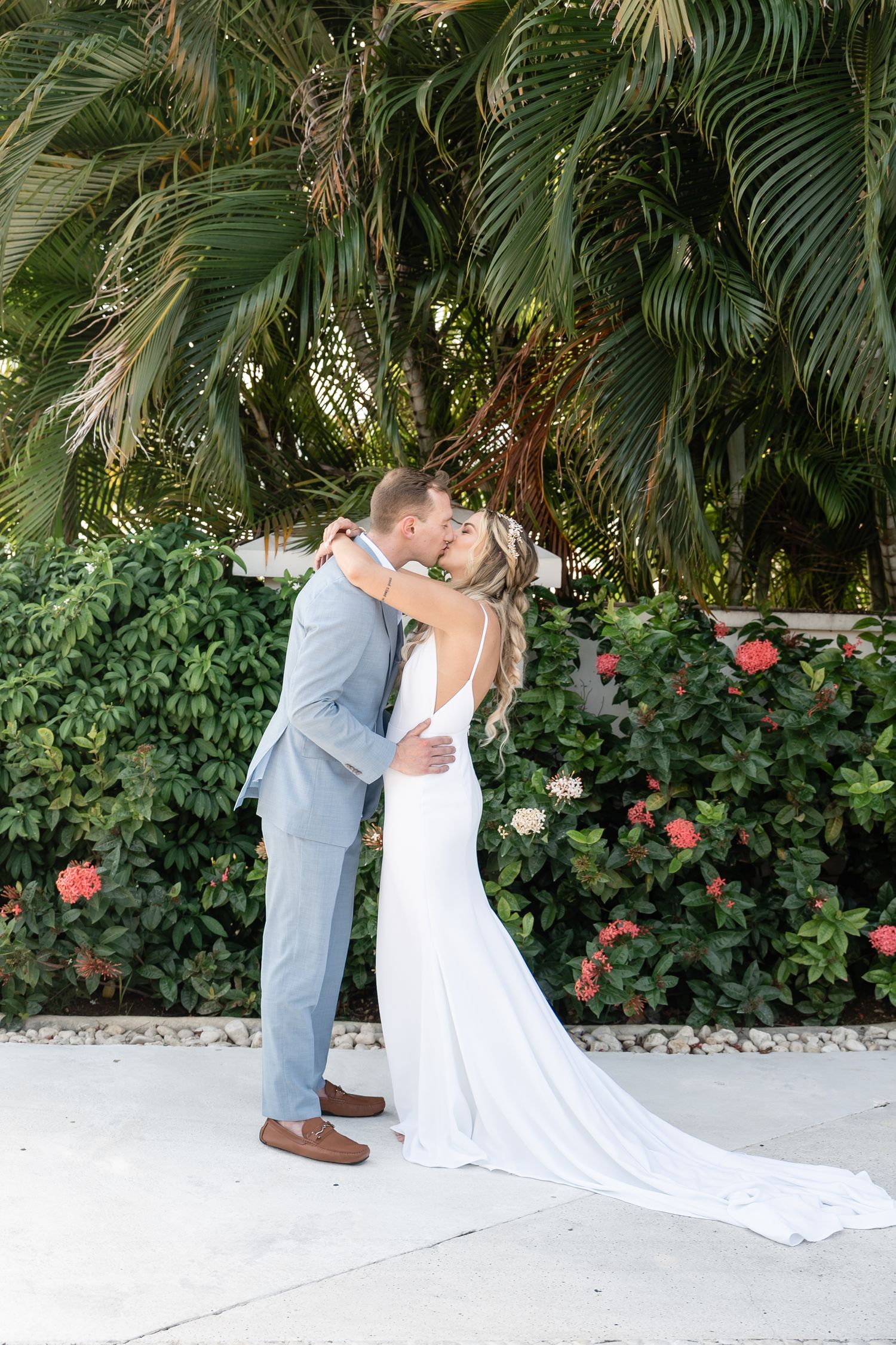 A romantic wedding moment captured in front of lush palm trees and flowering bushes.