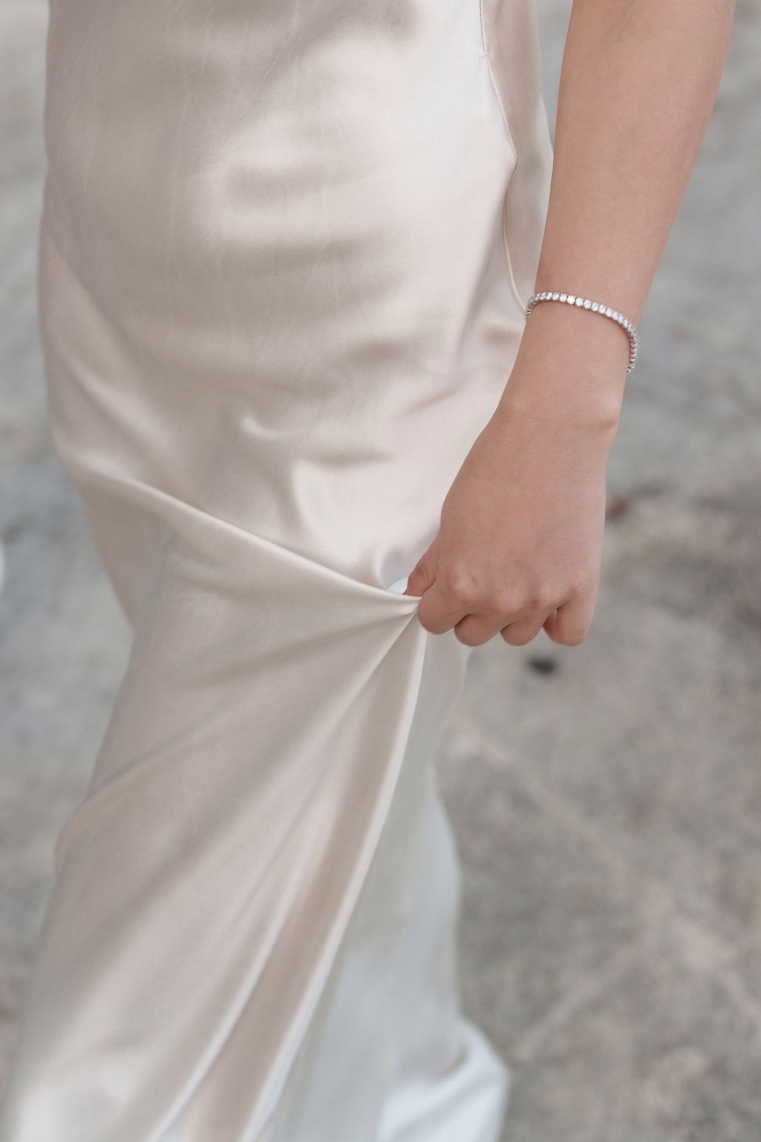 Detail of an elegant white silk wedding dress with a delicate pearl bracelet.