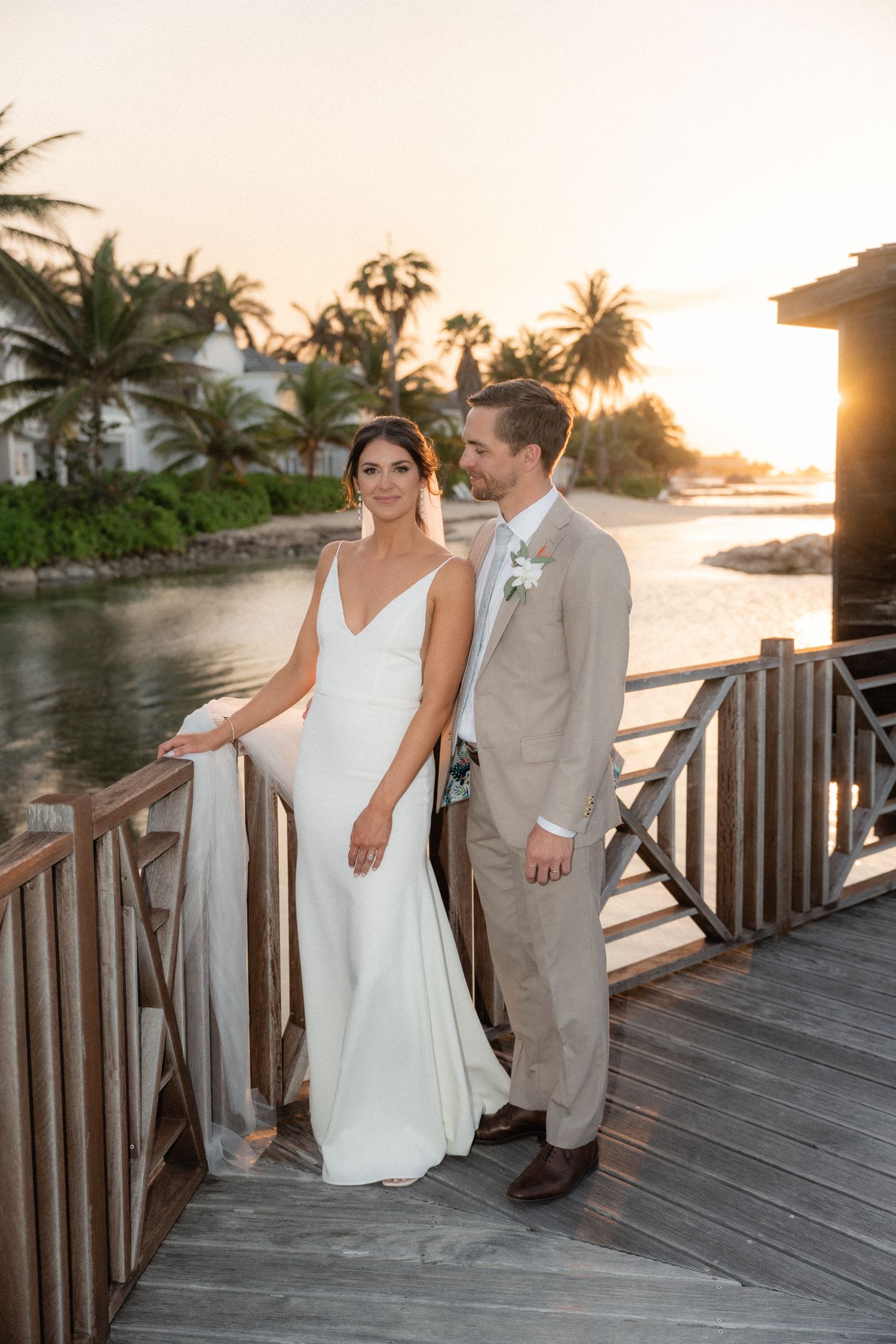 Sunset wedding portrait on a wooden deck overlooking tropical waters and palm trees.