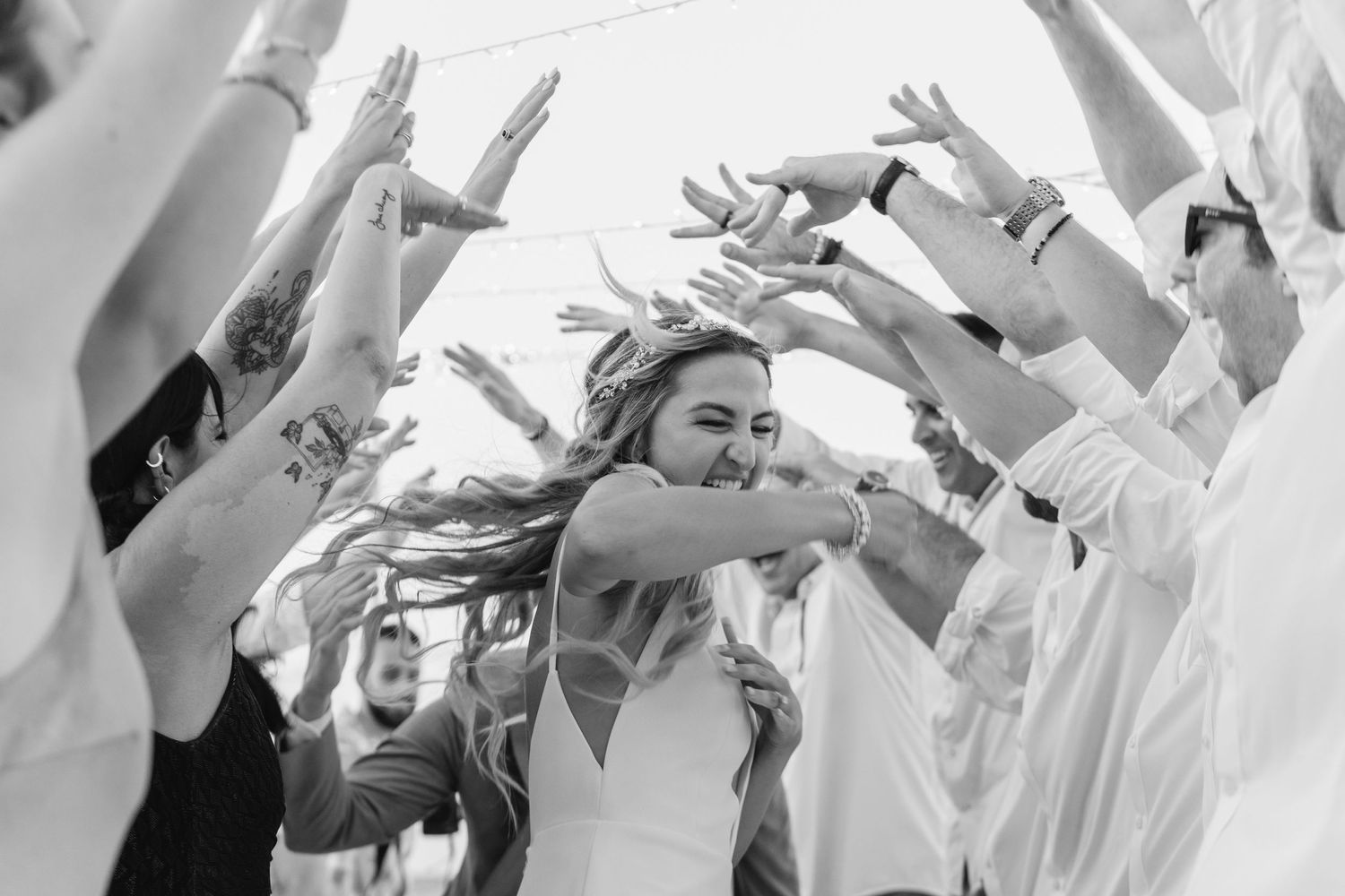 Black and white photo of celebratory dance with raised hands at wedding reception.