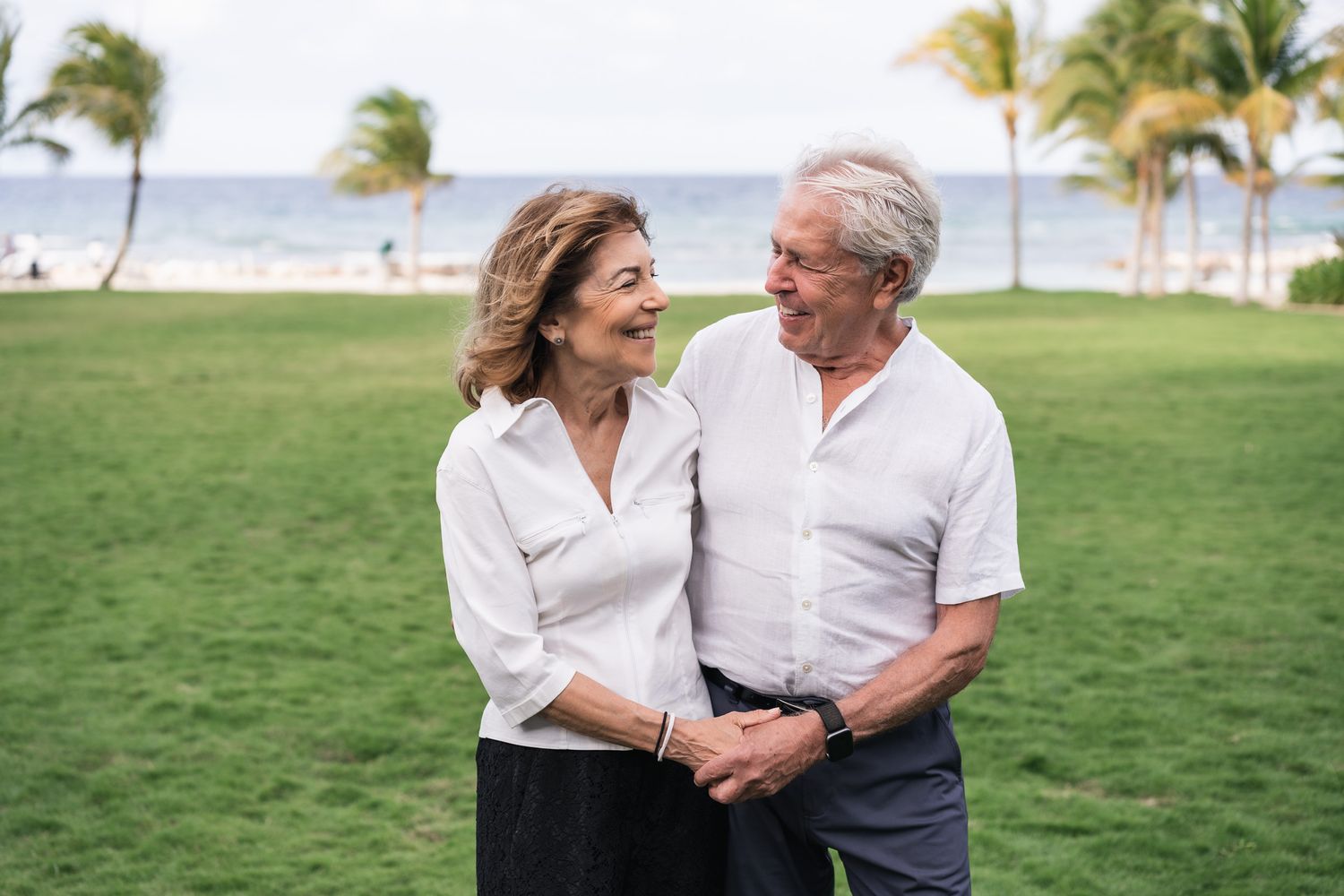 Couple shares an intimate moment on a palm-tree lined lawn by the ocean.