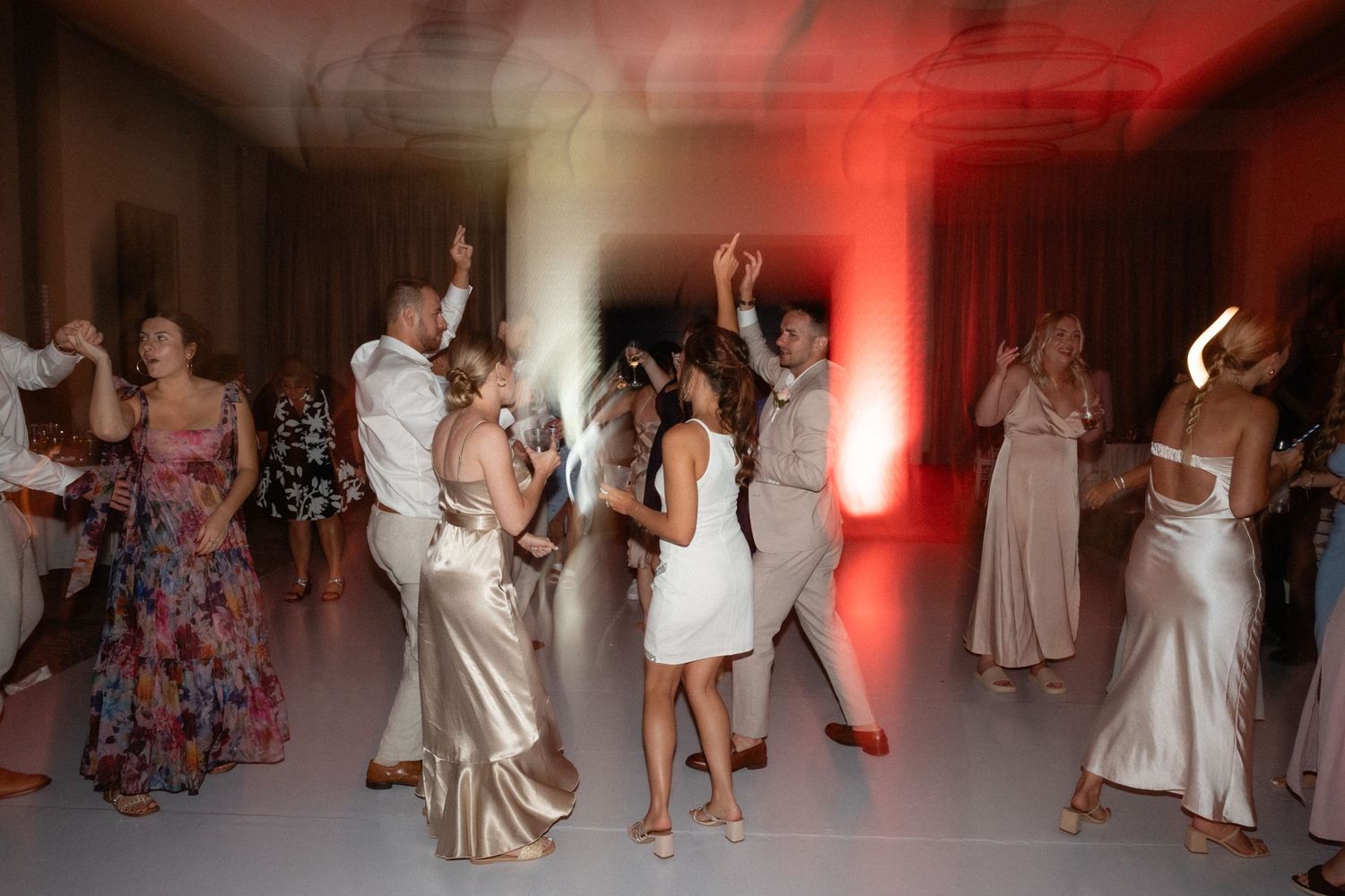 Wedding party dancing and celebrating in a reception hall with dramatic red lighting.
