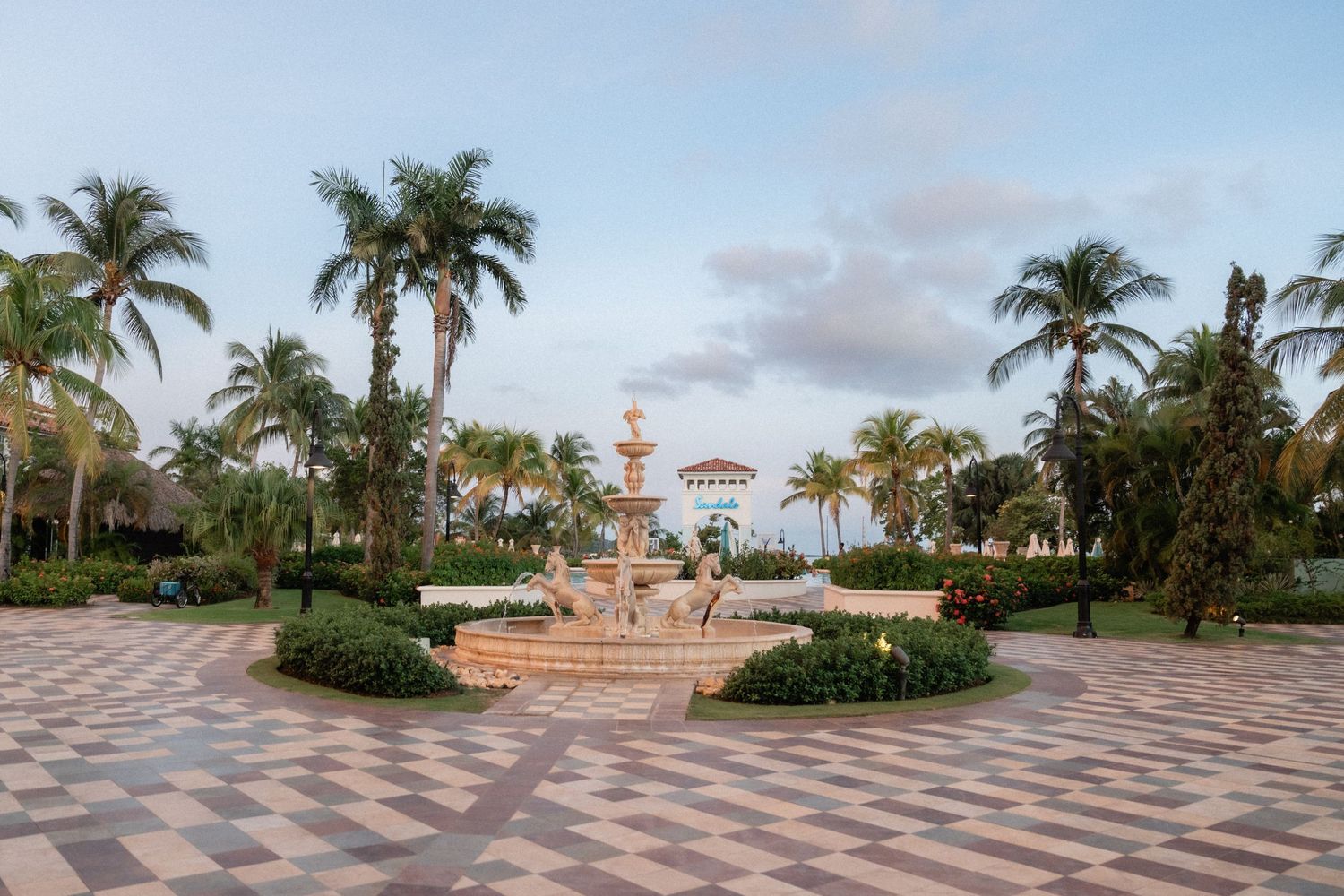 Elegant outdoor courtyard with a decorative fountain surrounded by palm trees and patterned stone pavement.