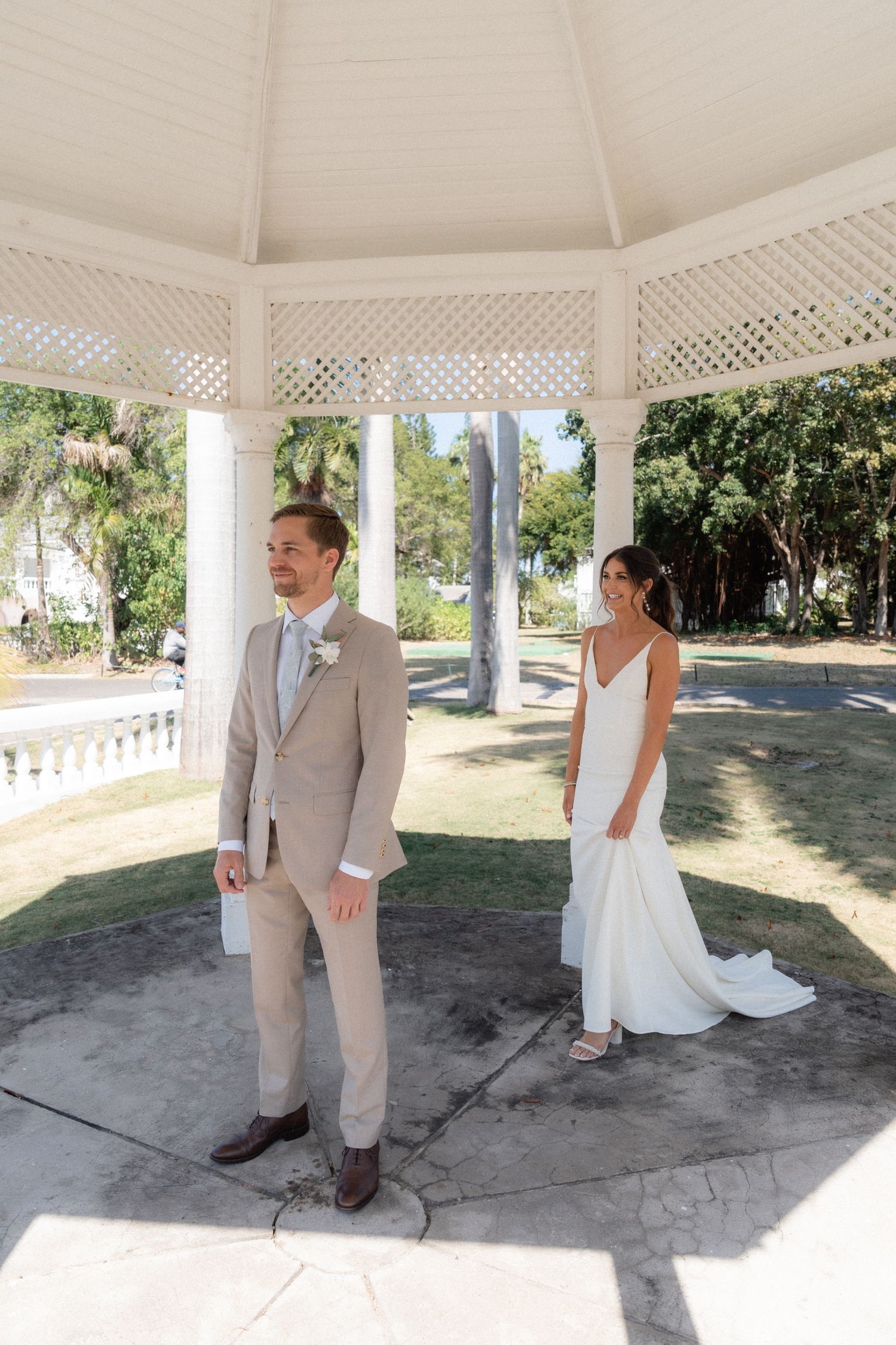Couple shares first look moment in white gazebo surrounded by palm trees.