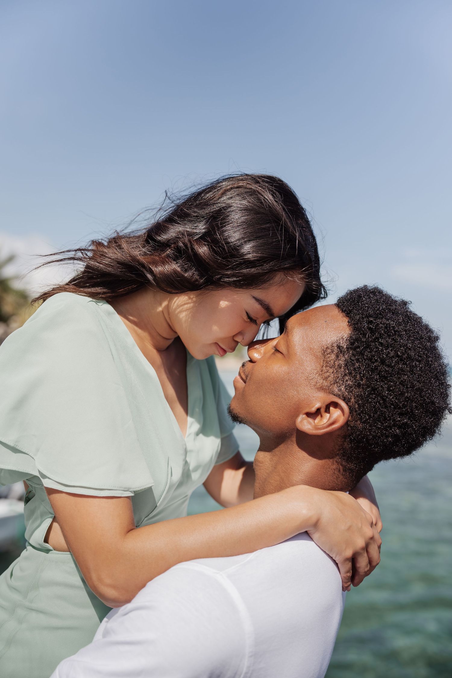A tender romantic moment captured between a couple against the backdrop of a blue ocean.
