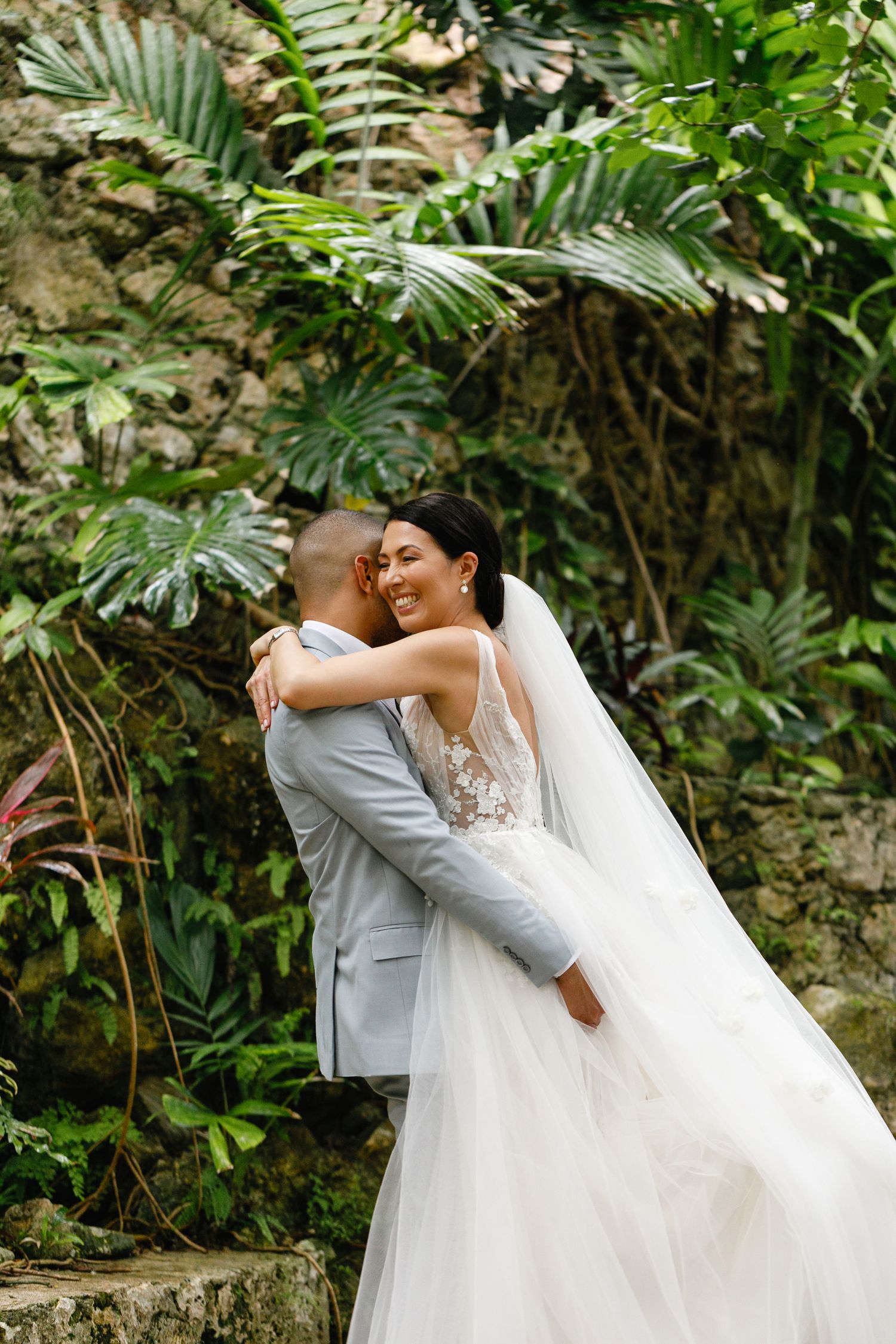Bride embraces groom, smiling joyfully, surrounded by lush tropical greenery, photographed by PhotoMagic Studio at Couples Sans Souci