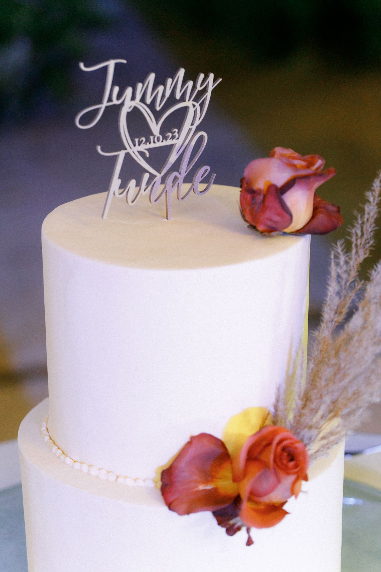 Elegant white wedding cake decorated with orange roses and a personalized topper.