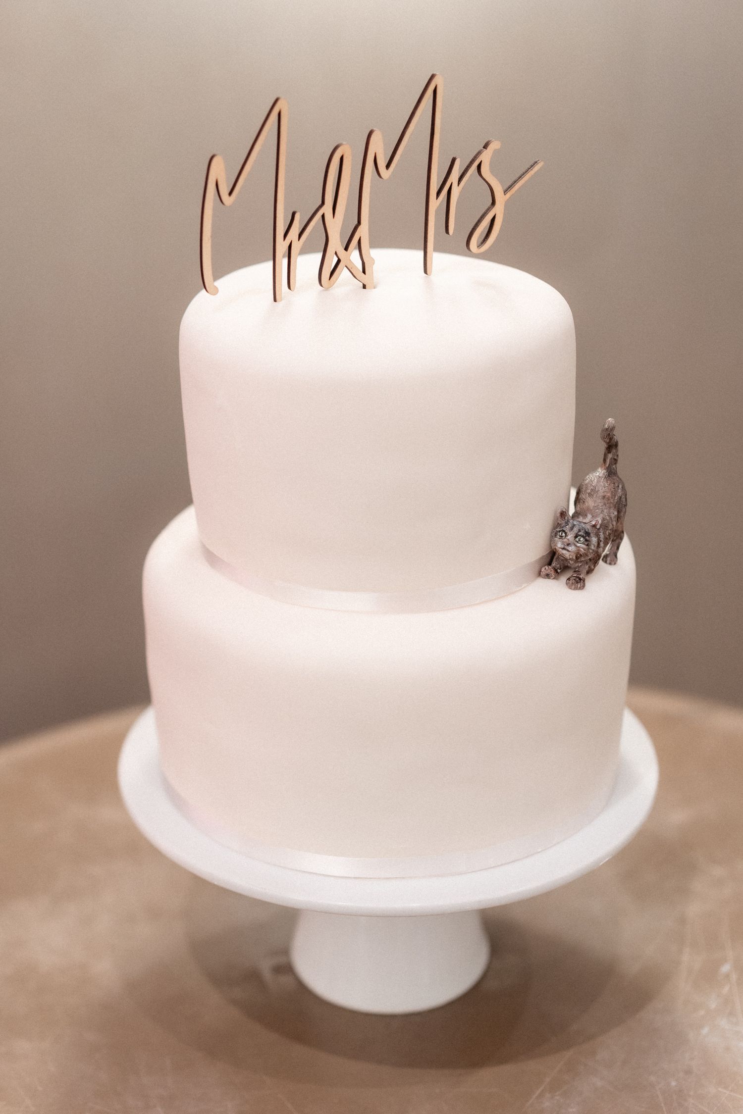 A minimalist two-tier white wedding cake with gold 'Mr & Mrs' cake topper.