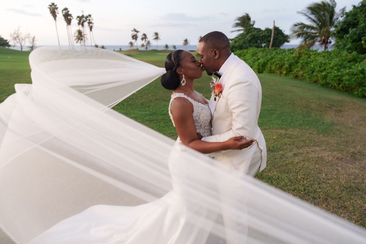 Romantic beach wedding portrait with flowing veil caught in ocean breeze.