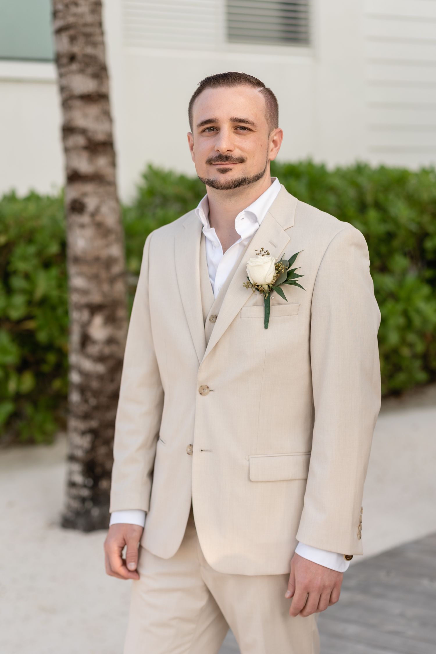 Formal portrait of groom in light beige suit with white boutonniere.