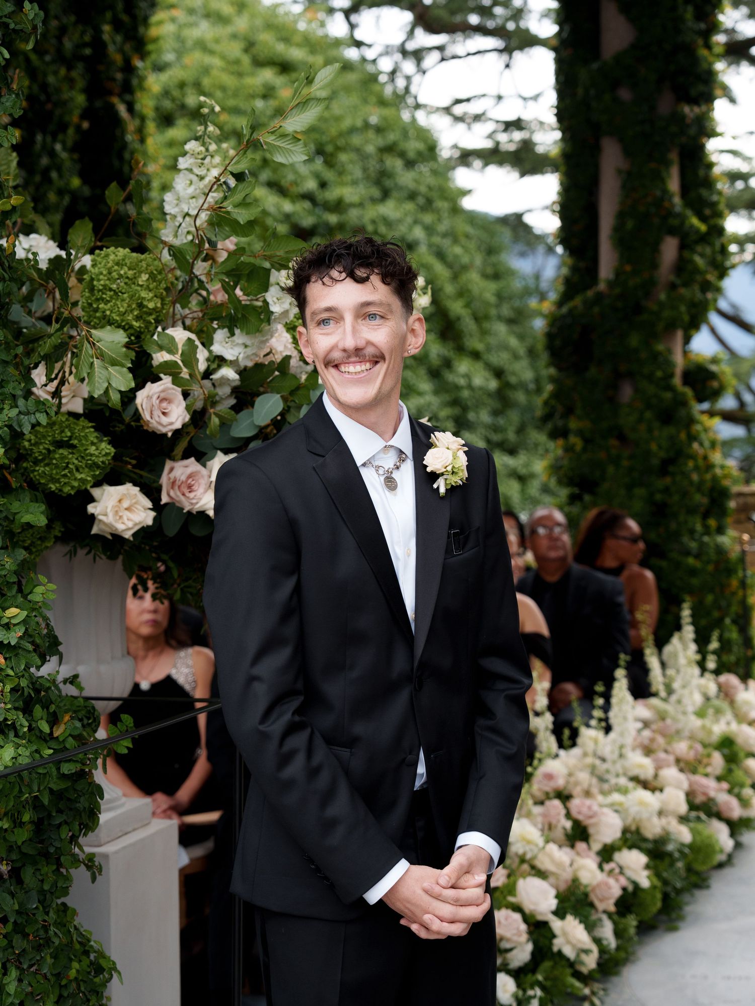 Wedding ceremony setup with white floral arrangements and elegant decor in a garden setting.