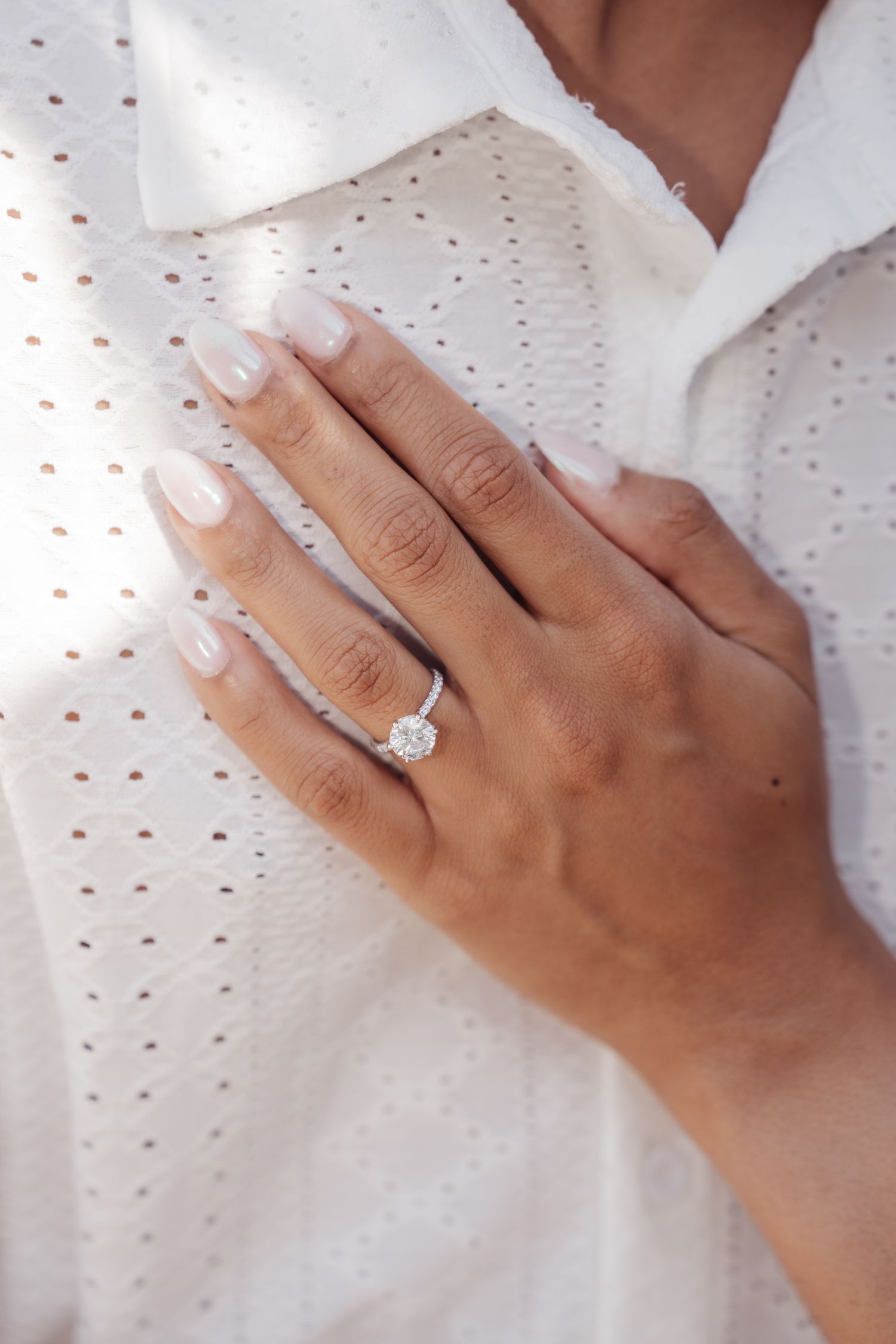 Close-up of an engagement ring on a hand against white eyelet fabric.