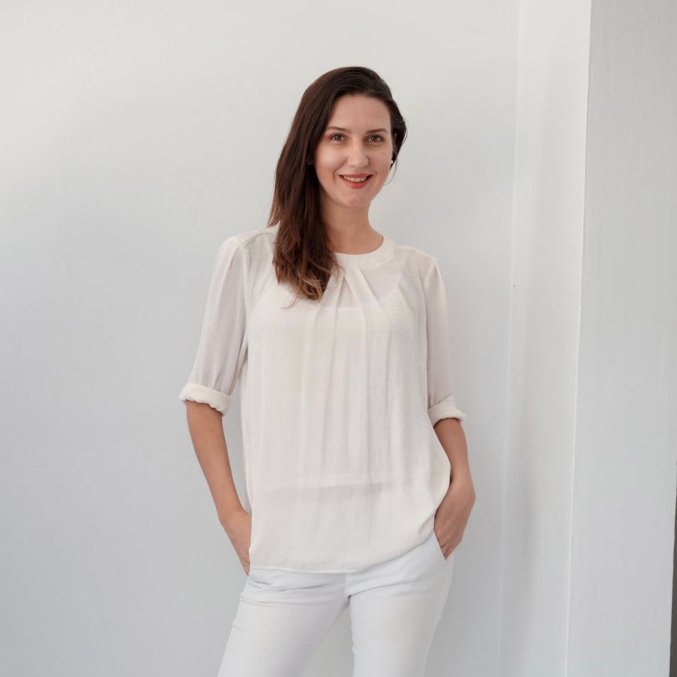 Person wearing white t-shirt and pants poses against white wall in minimalist fashion series.