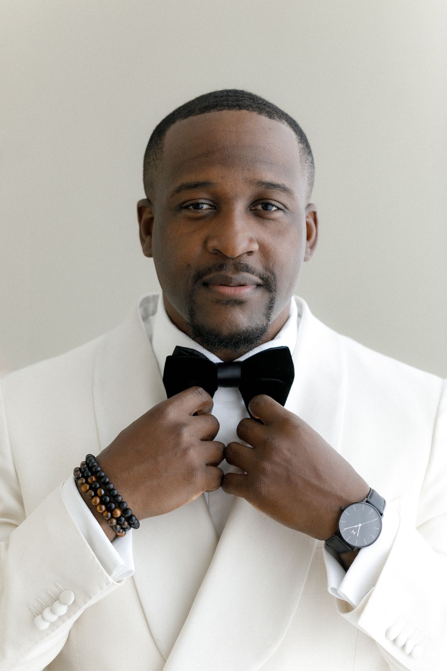 Formal portrait in white tuxedo with black bow tie and elegant accessories.