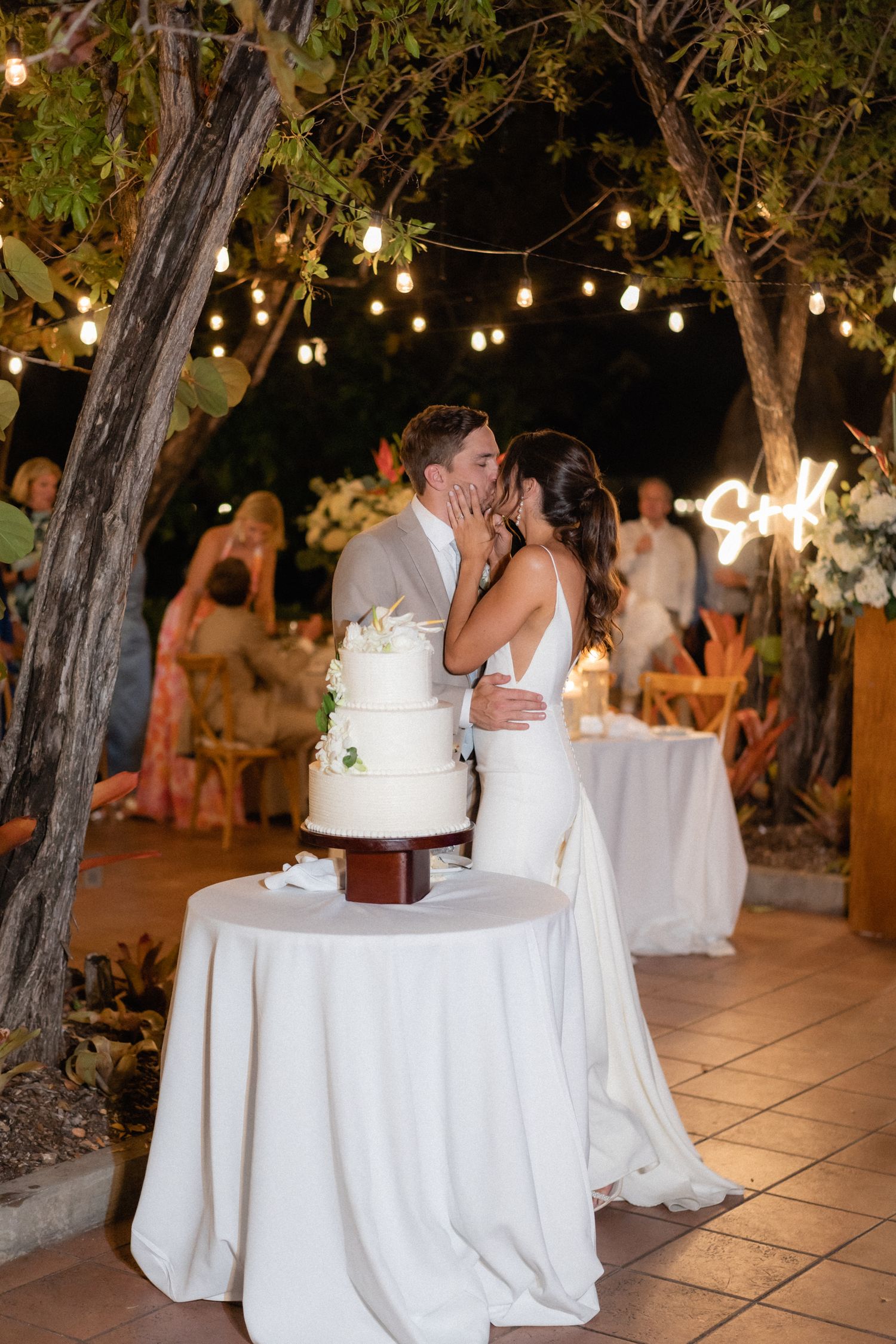 Couple shares intimate moment while cutting their wedding cake at outdoor evening reception.