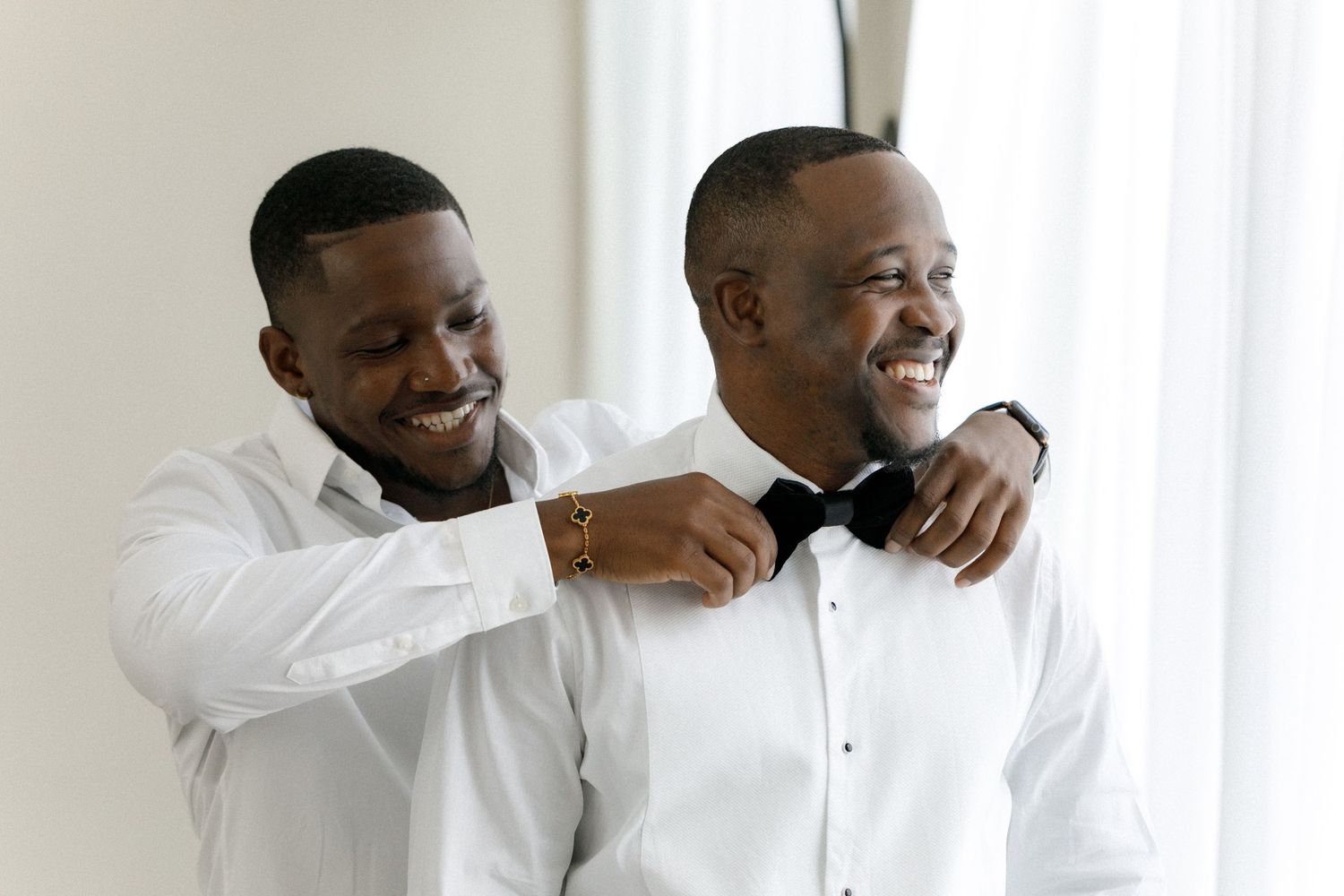 Getting ready moment with formal wear adjustments in bright white room.