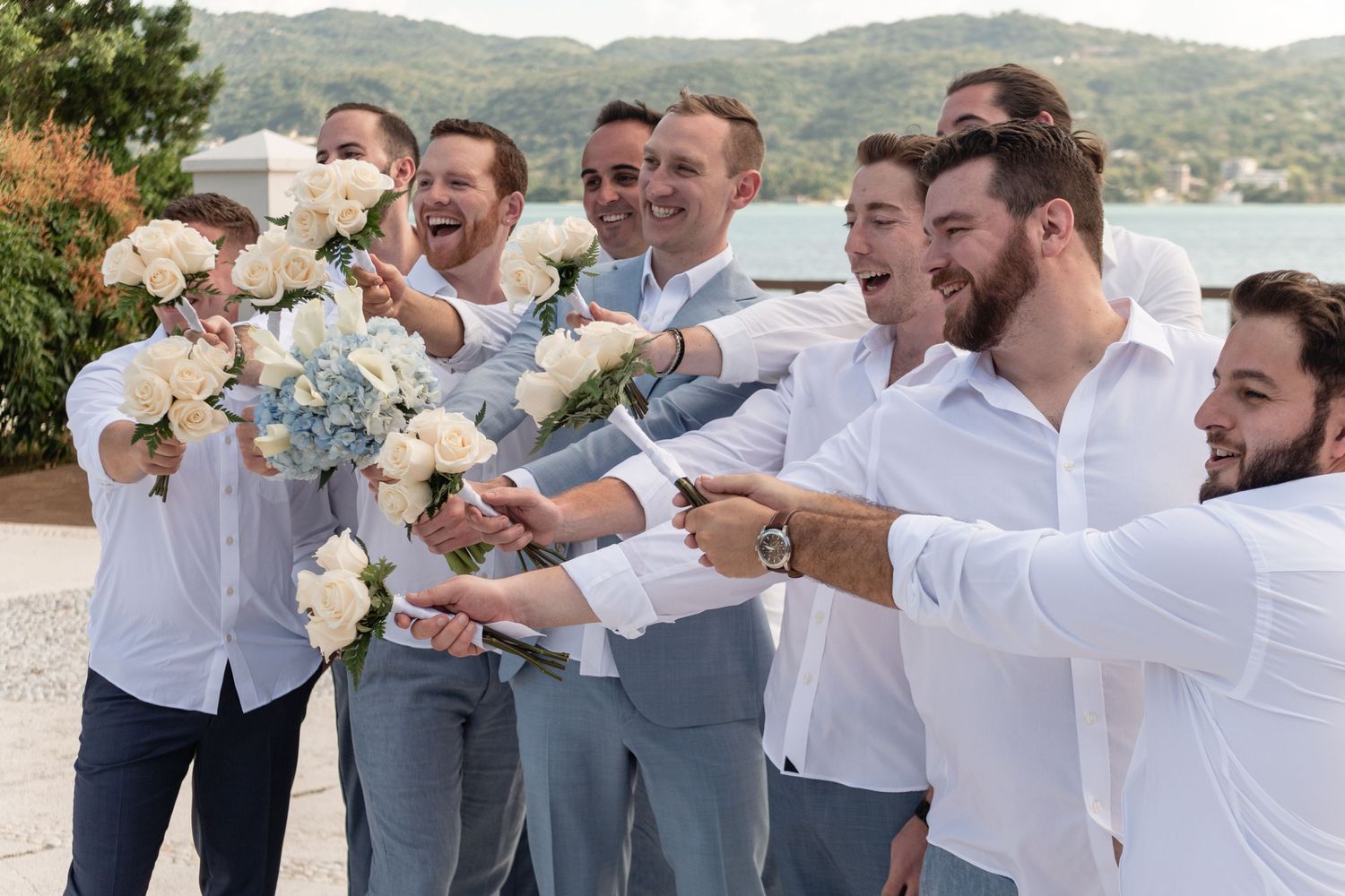 Wedding party in white shirts and gray pants celebrating with champagne bottles at an outdoor venue.