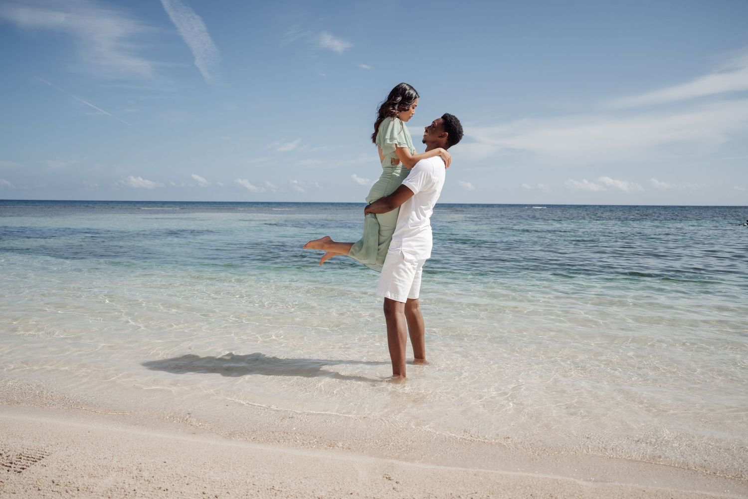 A joyful couple plays on the beach as one lifts the other in a celebratory moment.