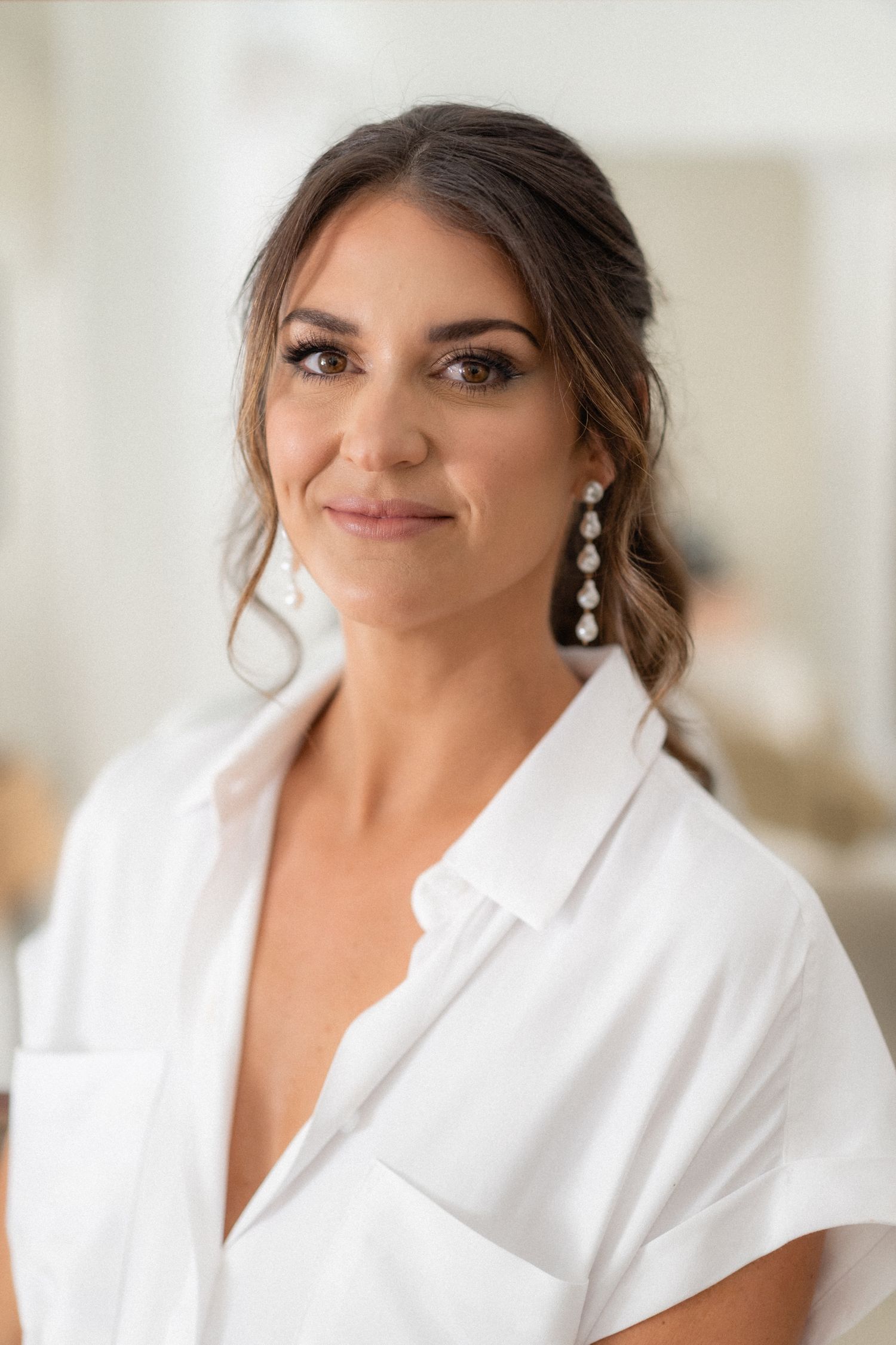 Portrait of someone wearing a white robe and elegant drop earrings while getting ready.
