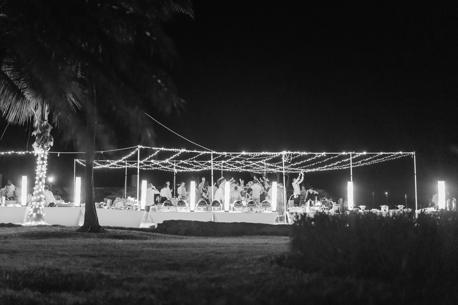 A nighttime outdoor wedding reception setup with string lights illuminating a tent structure on a dark evening.