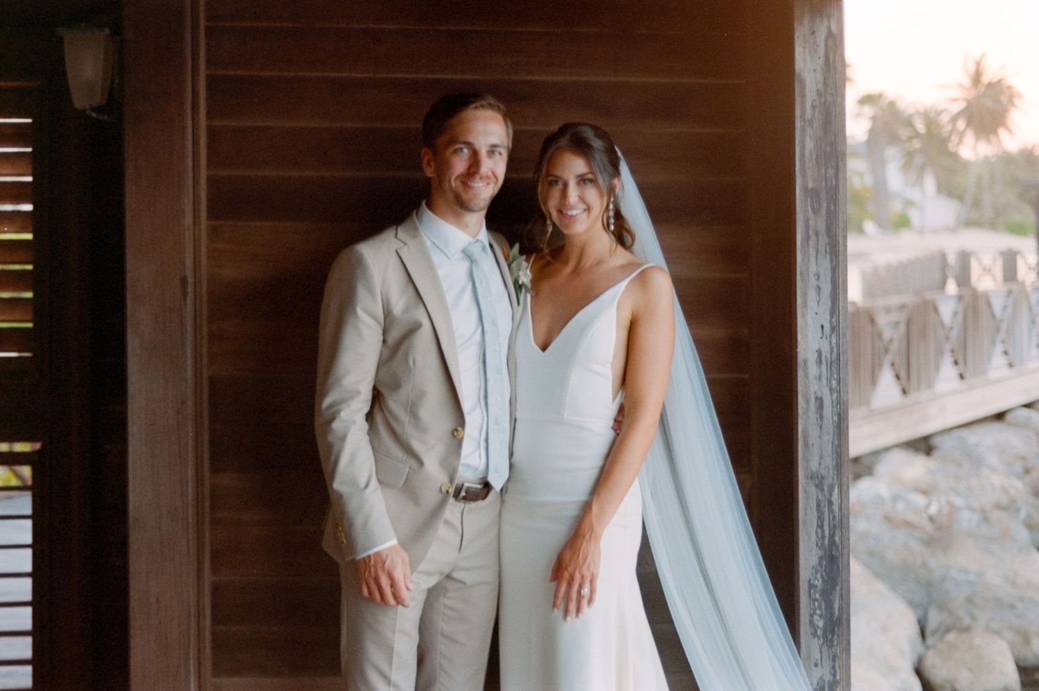 A couple in wedding attire poses in an elegant doorway wearing light colored formal wear.