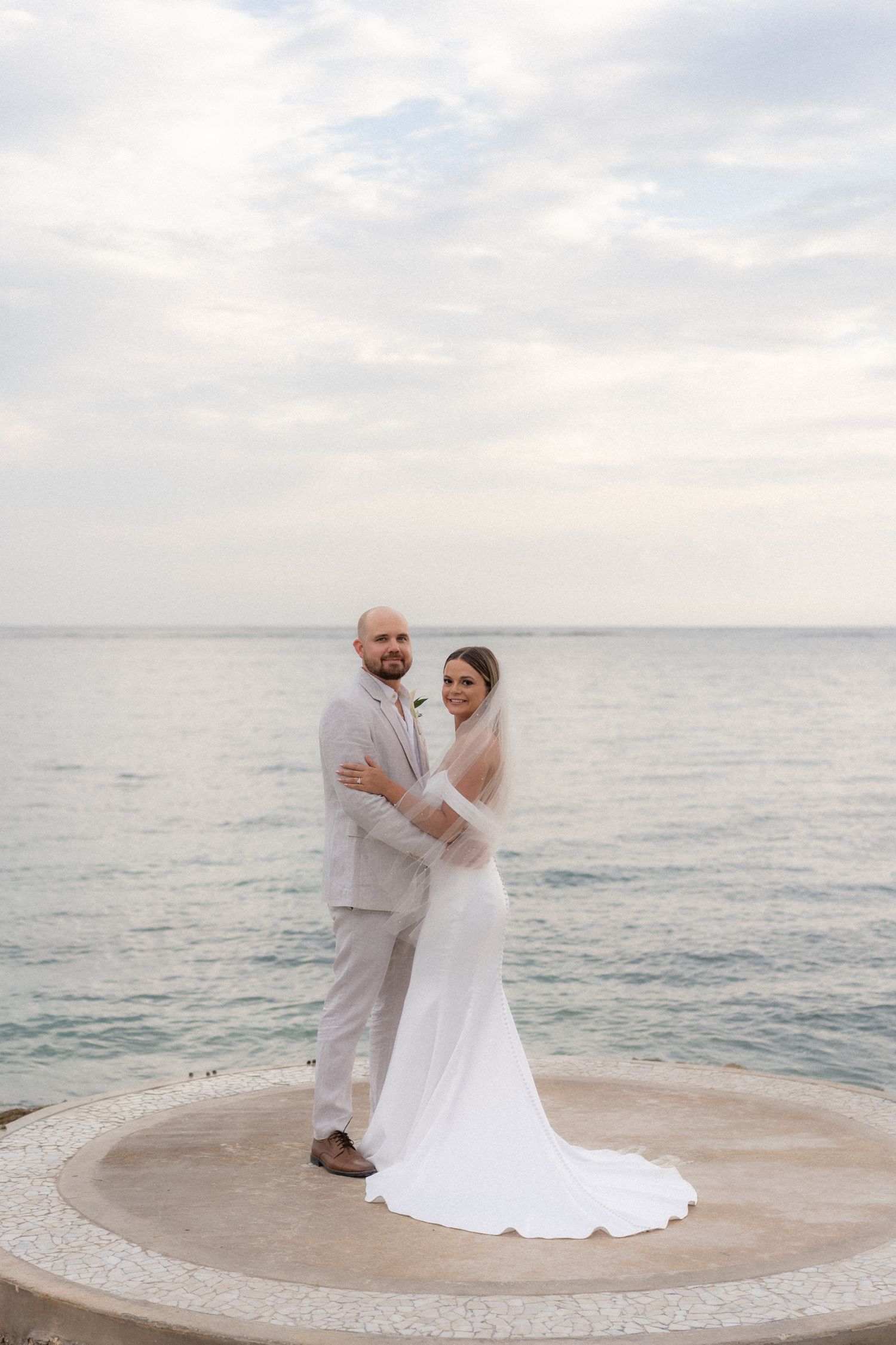 Romantic coastal wedding portrait on a circular platform overlooking the ocean.