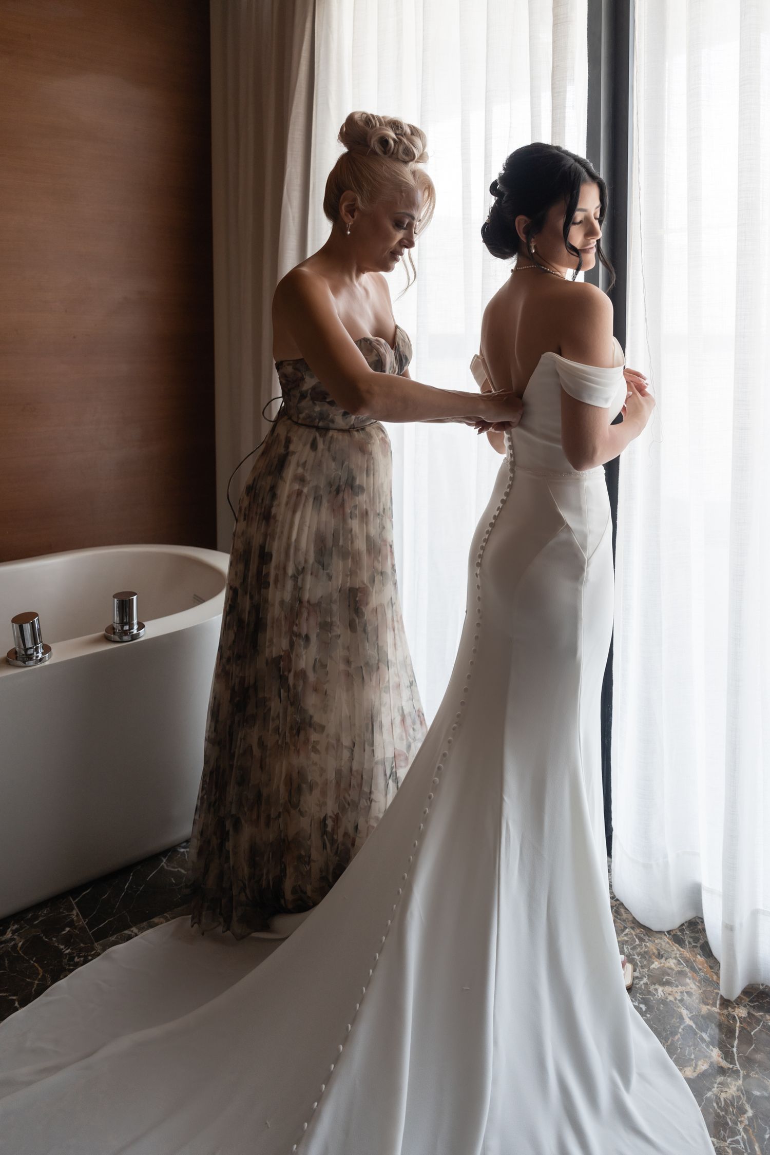 Wedding preparation scene showing final adjustments being made to an elegant white bridal gown.