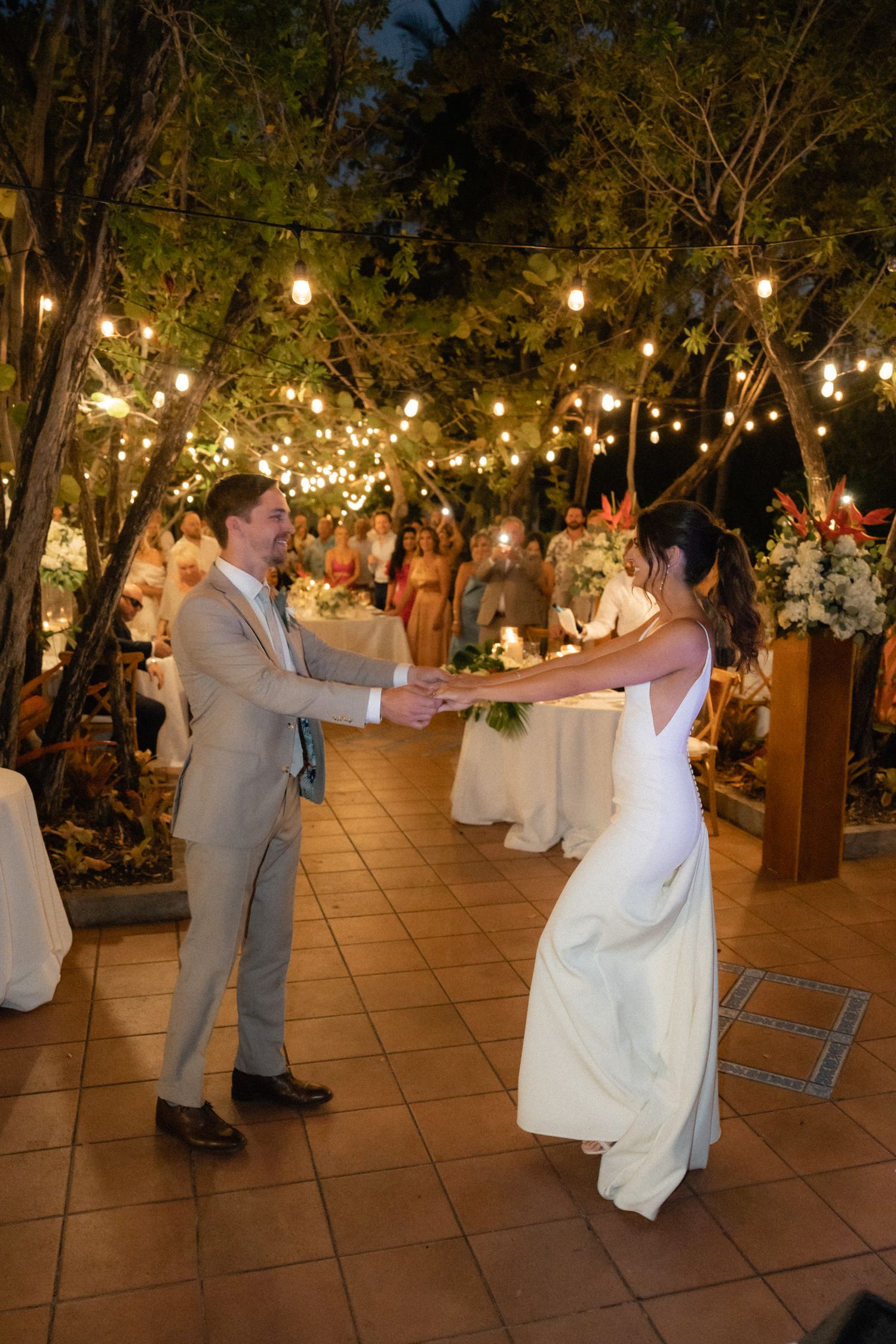 A couple shares their first dance under twinkling lights at an outdoor reception.