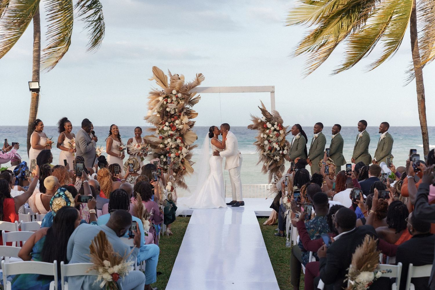 Elegant outdoor wedding ceremony by the ocean with decorative arch and seated guests.