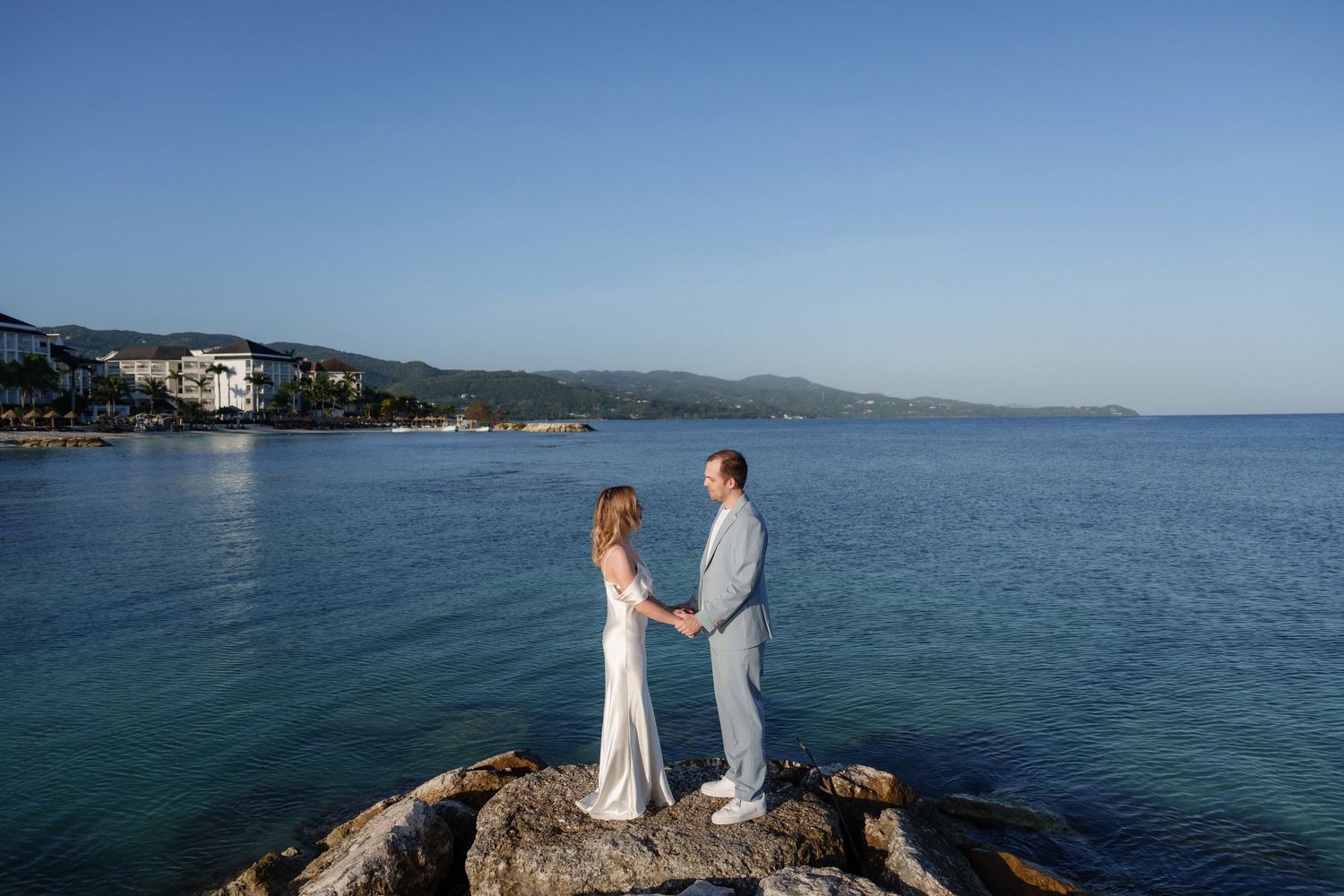 Couple standing on rocky outcrop with panoramic ocean and coastline views.