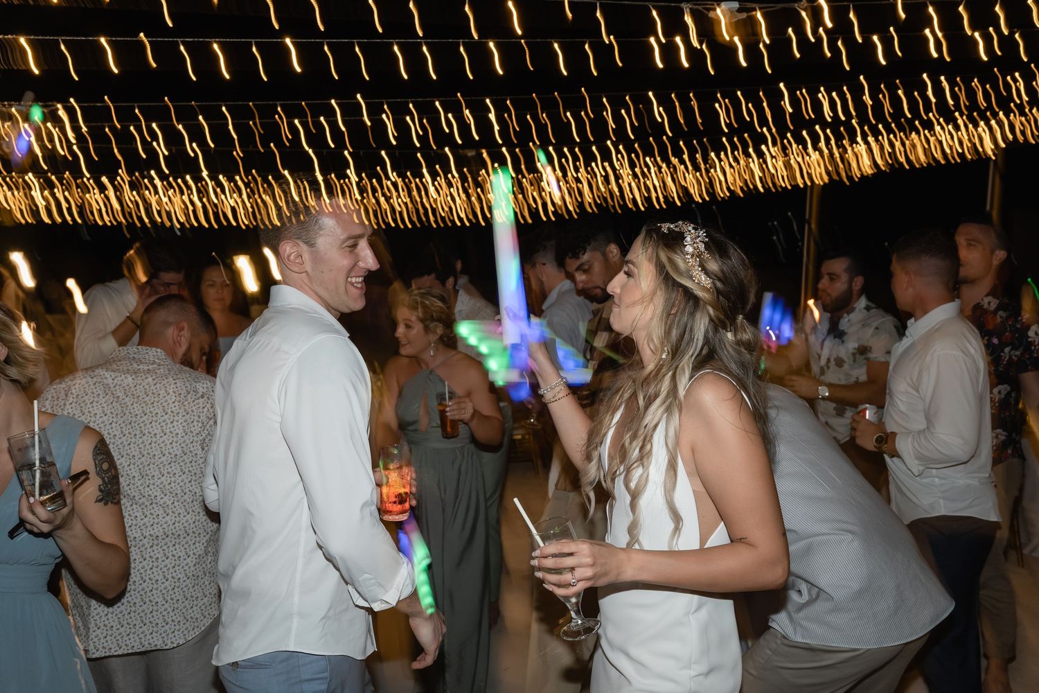 Party guests celebrating with LED glow sticks under twinkling lights at a nighttime event.