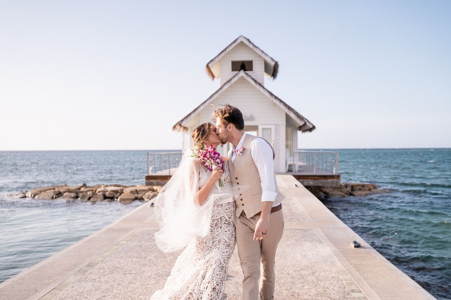 A romantic wedding portrait at a white seaside chapel with crashing waves.