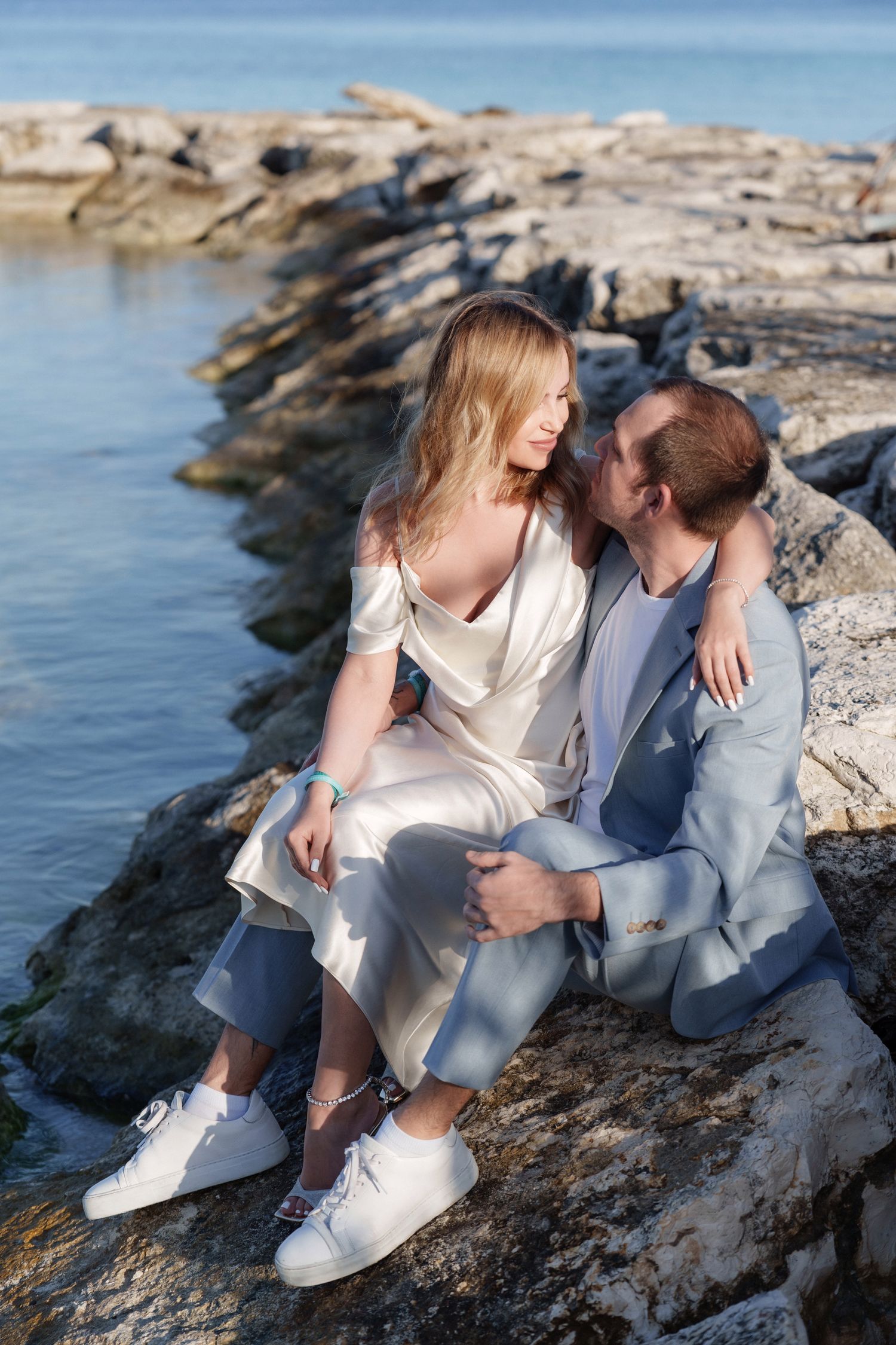 A romantic couple sitting on coastal rocks overlooking the Mediterranean sea.