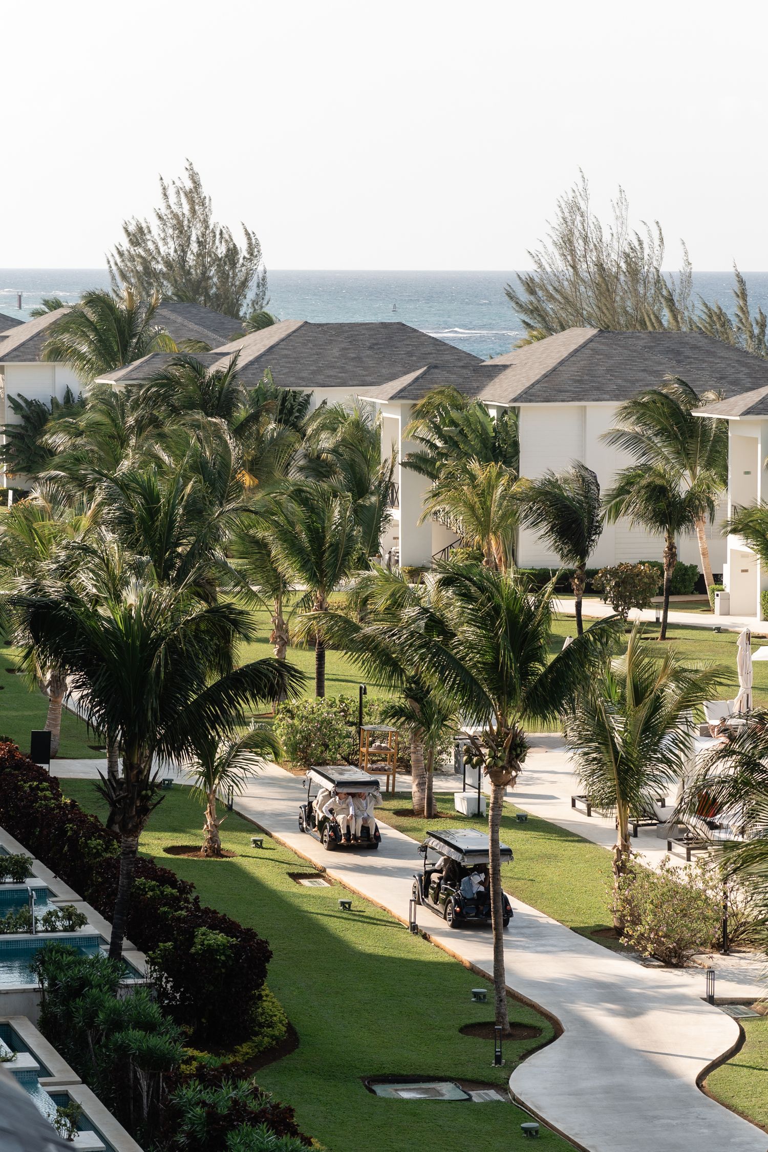 Tropical resort property with palm trees and white buildings along a winding pathway near the ocean.