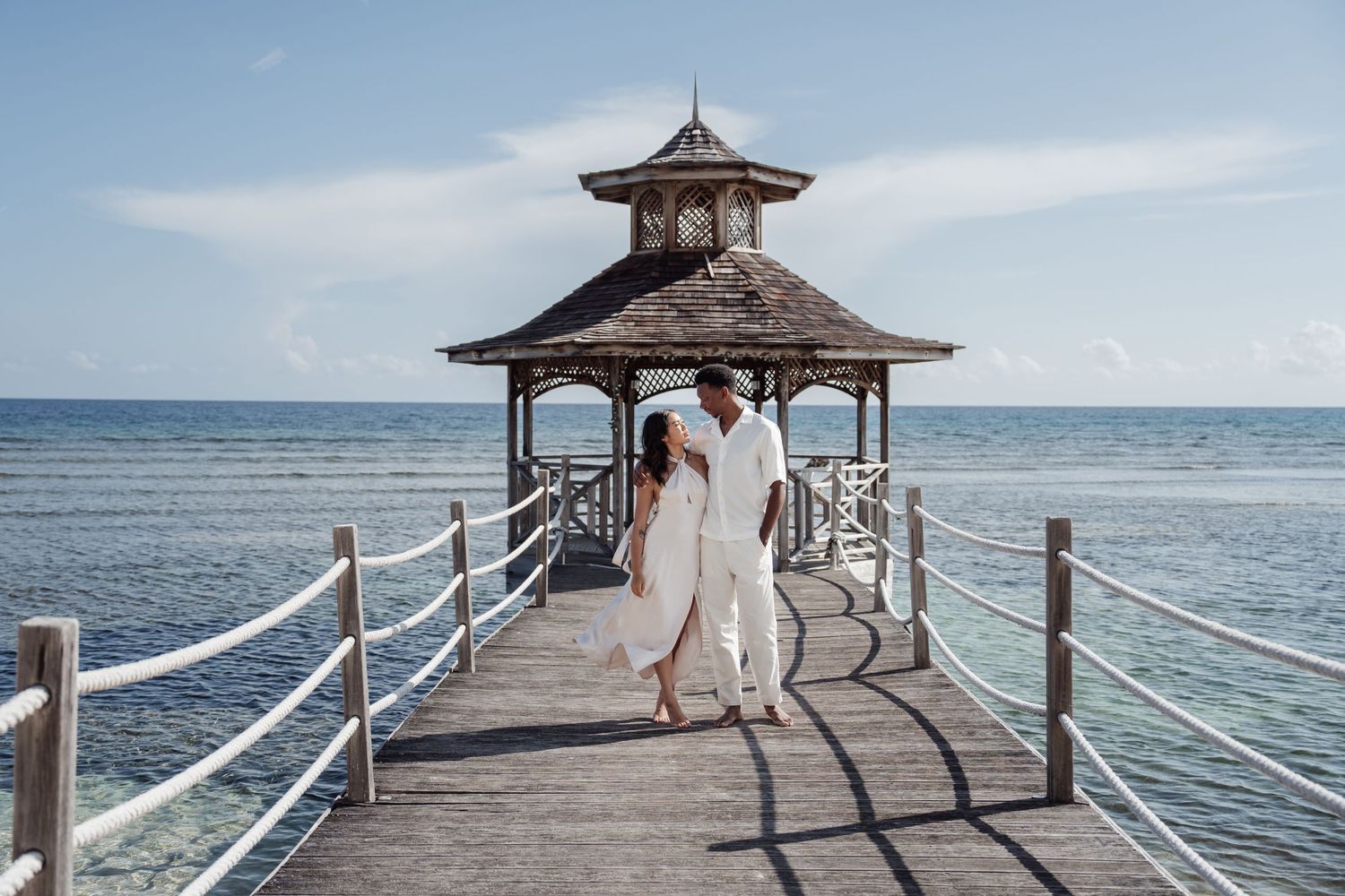 Couple walking on a wooden pier with gazebo overlooking the ocean.
