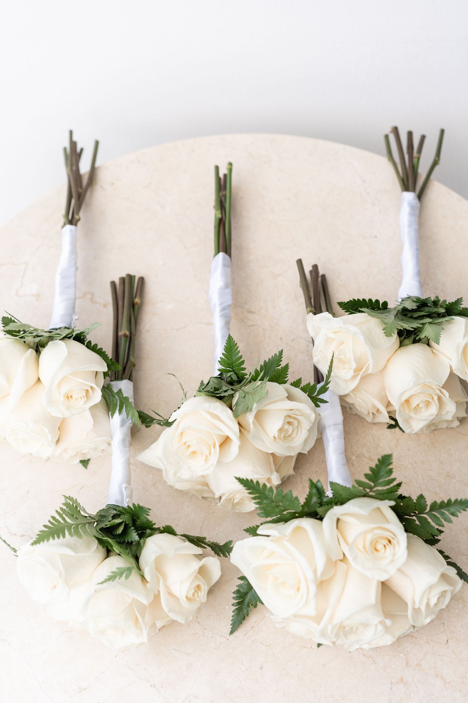 White rose boutonnieres wrapped in ribbon arranged on a neutral background.