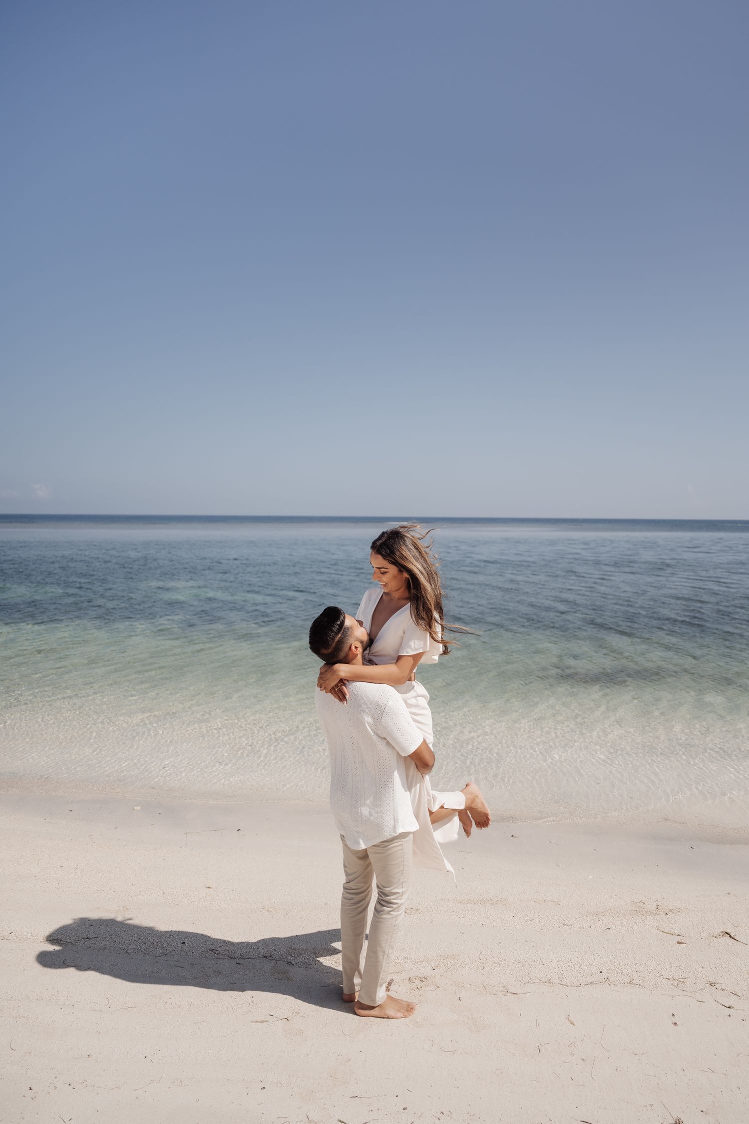 A joyful moment captured as a couple plays and lifts each other on a beautiful beach.