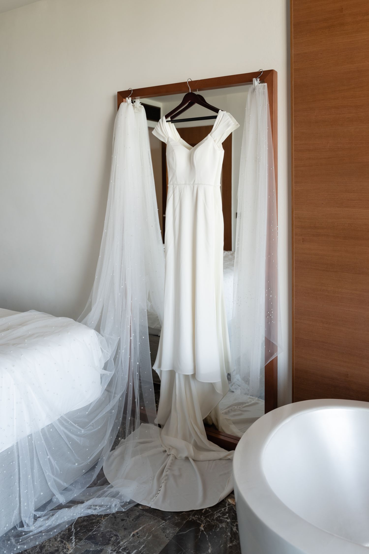 Elegant white wedding gown hanging on display with flowing veil in modern room.