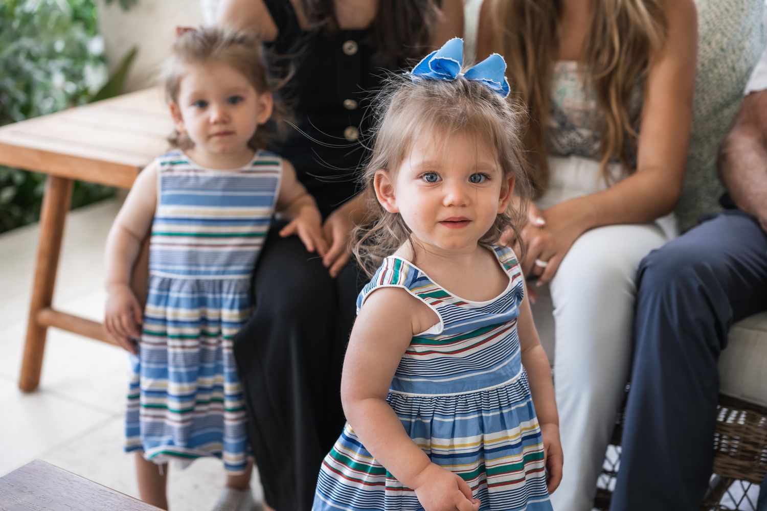 Two young girls in matching striped dresses pose on a porch.