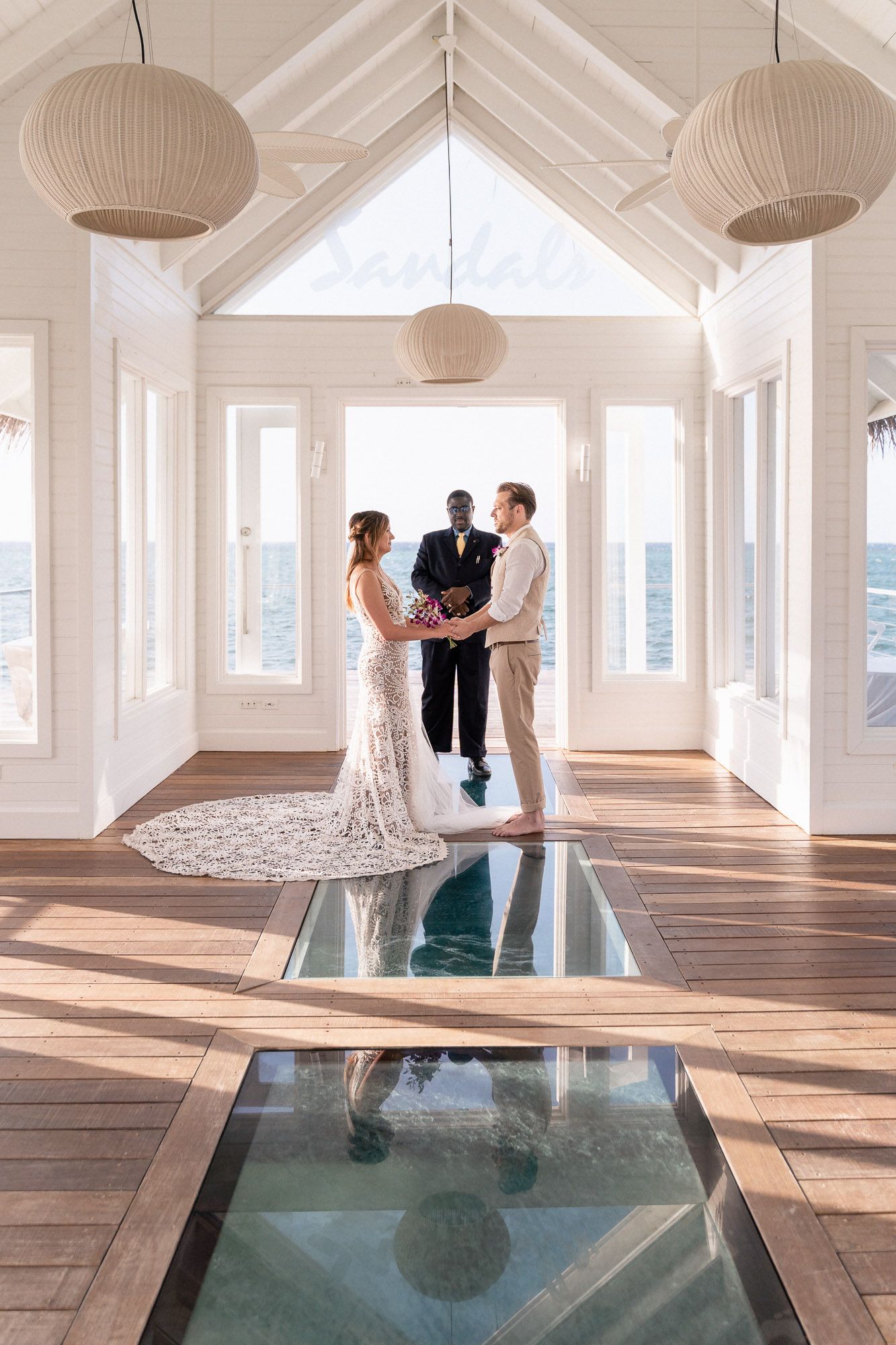 A wedding ceremony in a bright white chapel with glass floor panels and pendant lights.