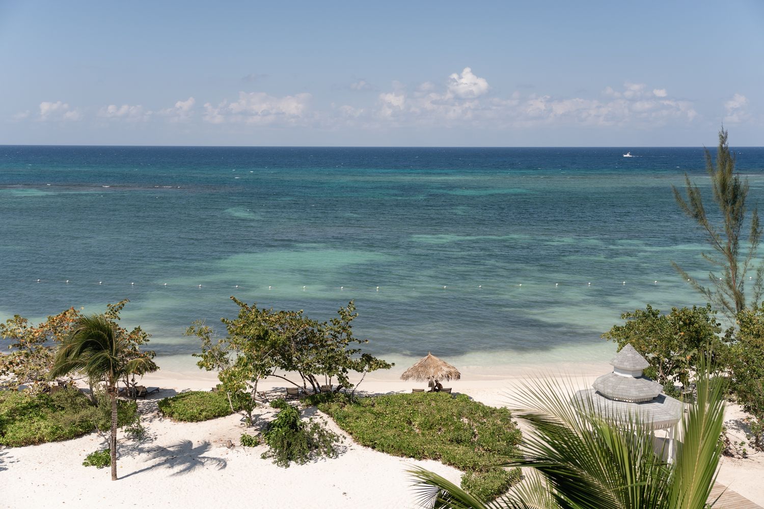 Turquoise ocean waters and white sandy beach viewed from a tropical resort with palm trees and umbrellas.