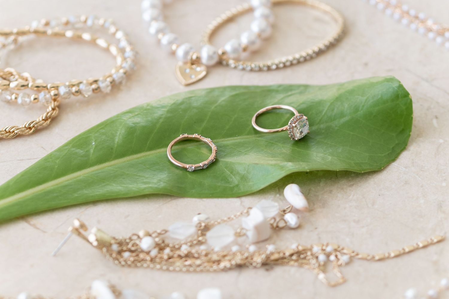 Wedding jewelry and rings displayed on green leaf with pearl accessories.