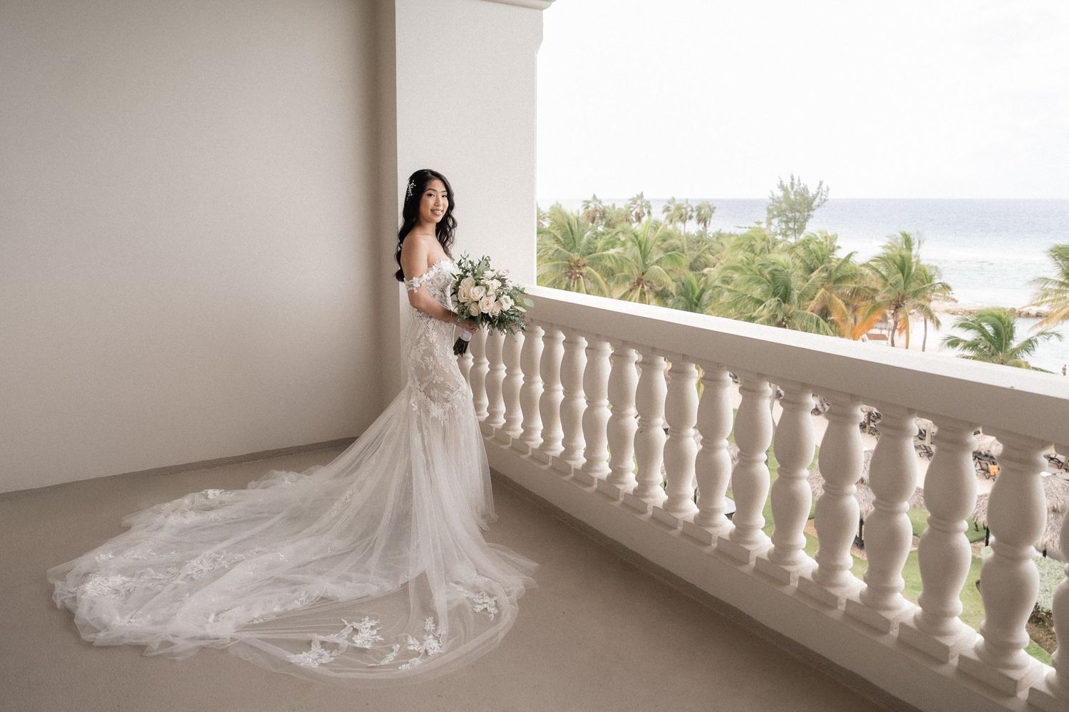 Elegant bridal portrait on a balcony with white columns and ocean view in the background.