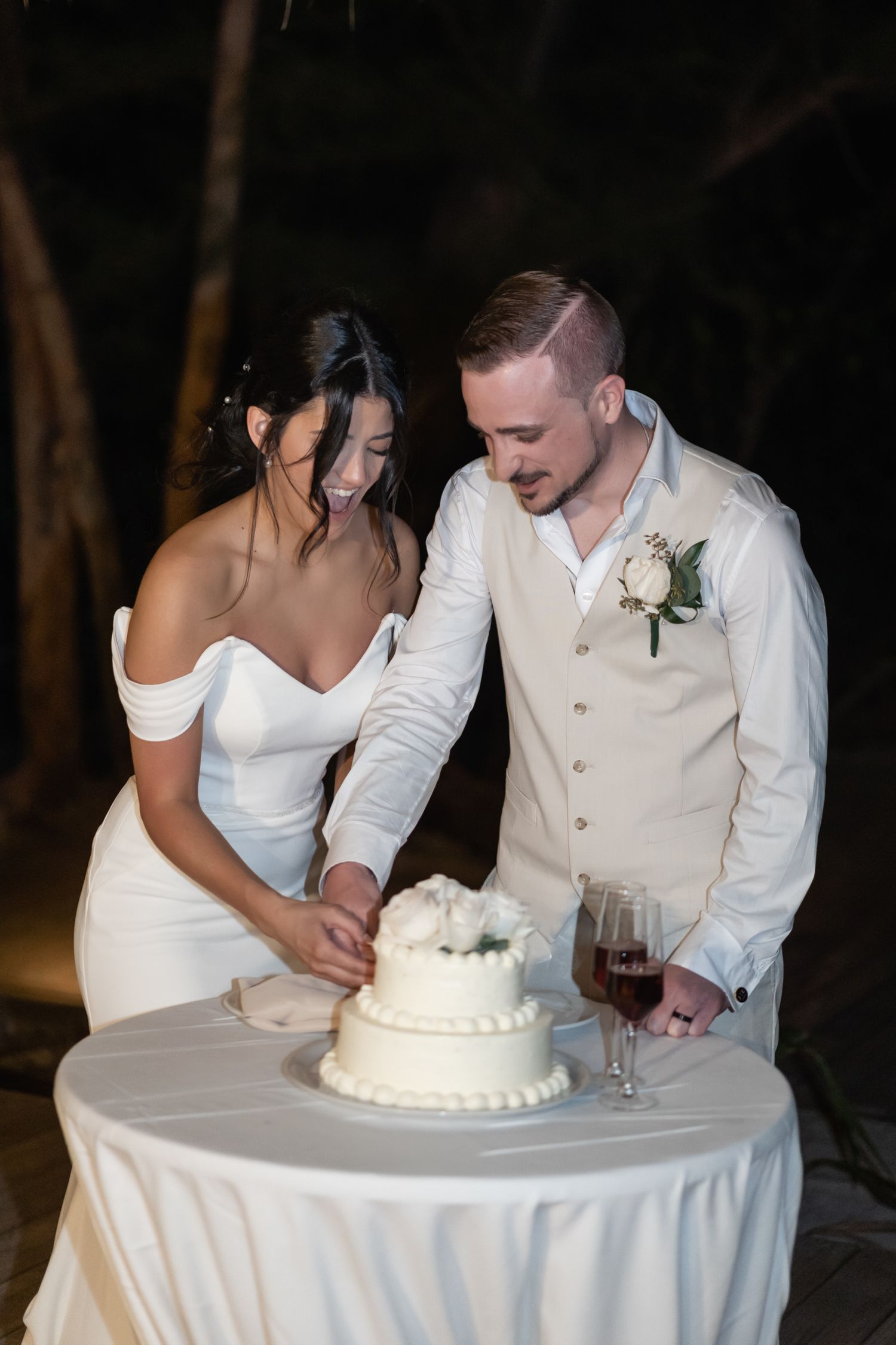 A wedding couple shares a joyful moment while cutting their white wedding cake at their reception.